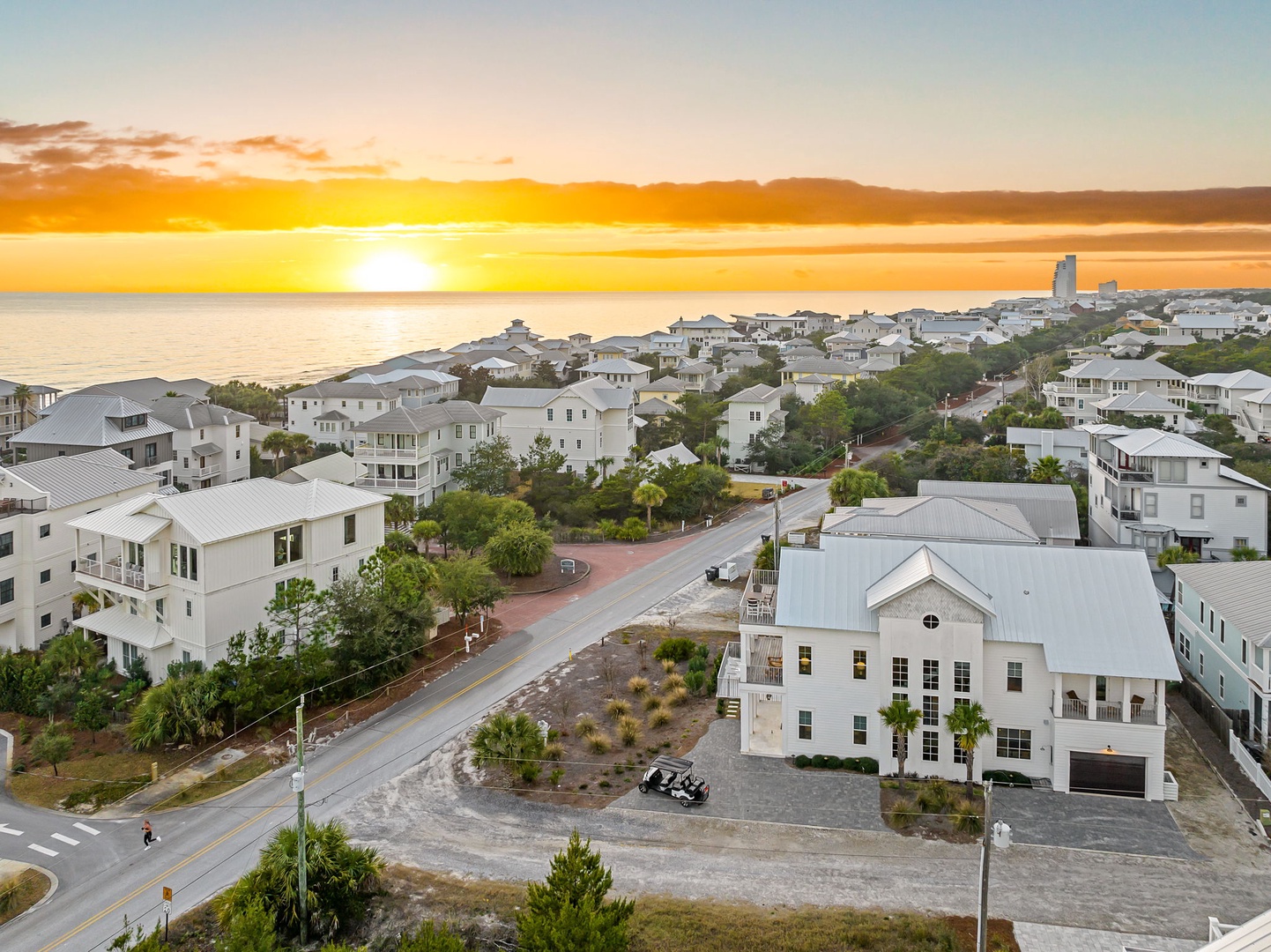Stunning aerial view captures the coastal community at sunset, with charming beach houses nestled along tree-lined streets near the waterfront.