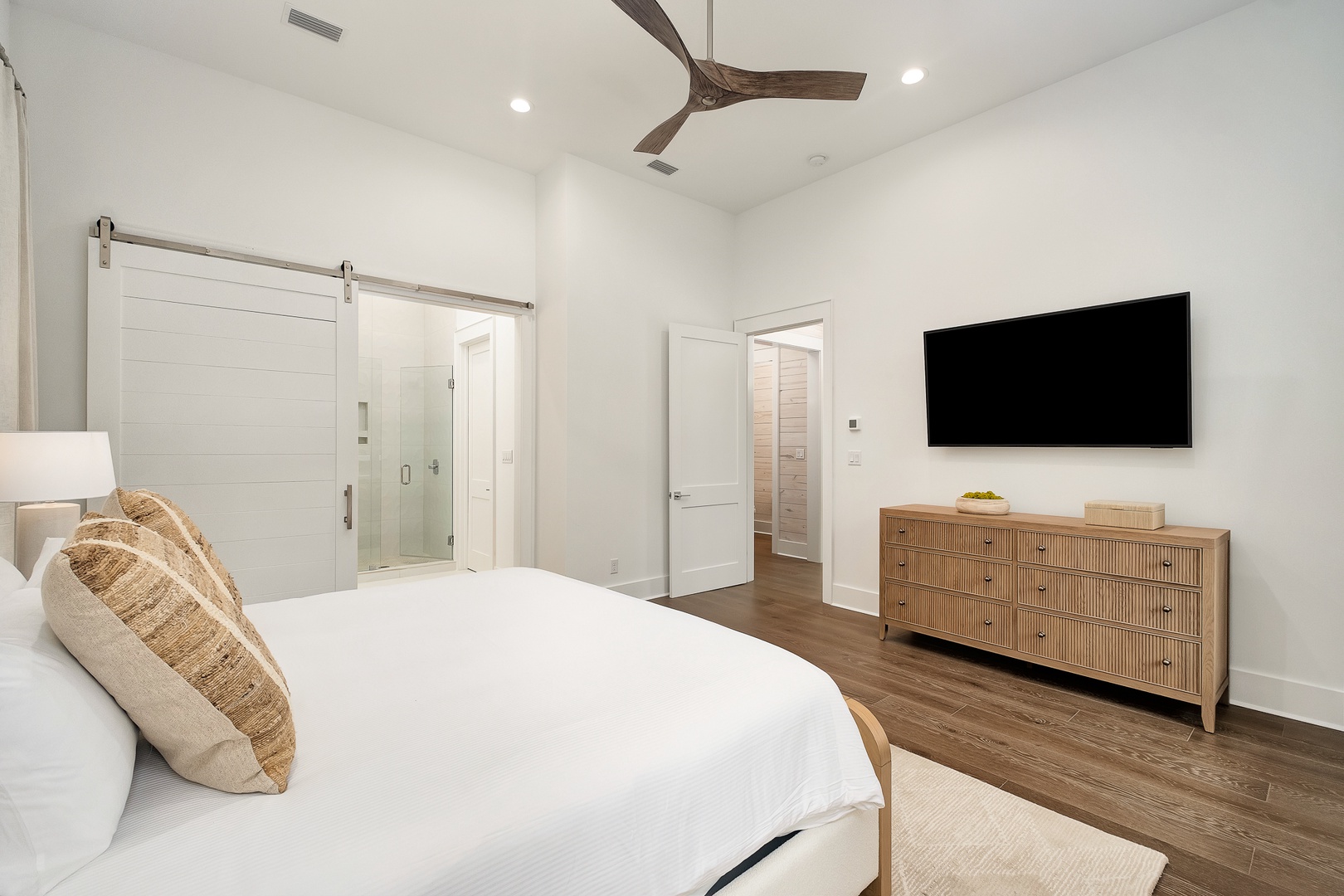 Unwind in your bright, modern bedroom featuring crisp white linens, warm wood accents, and a wall-mounted TV for cozy nights in.