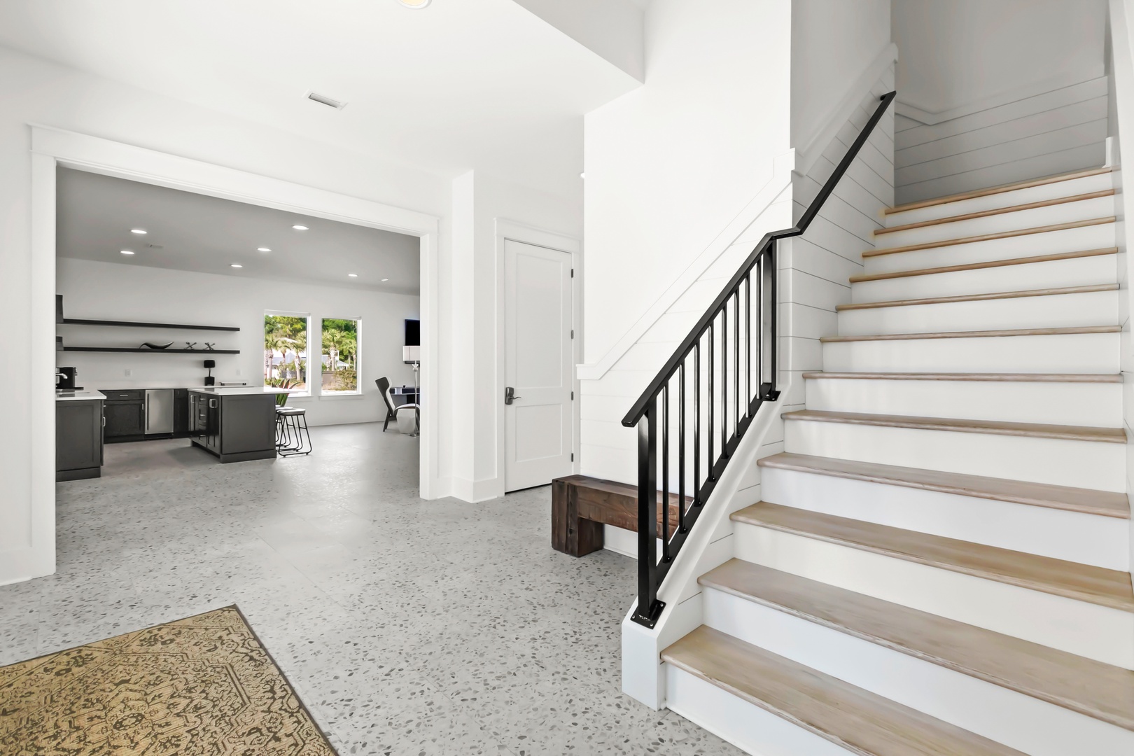 Step into your bright, open entryway where sleek modern design meets natural warmth. The staircase invites you upstairs, while the gourmet kitchen beckons beyond, all wrapped in clean white walls and sunlit charm.