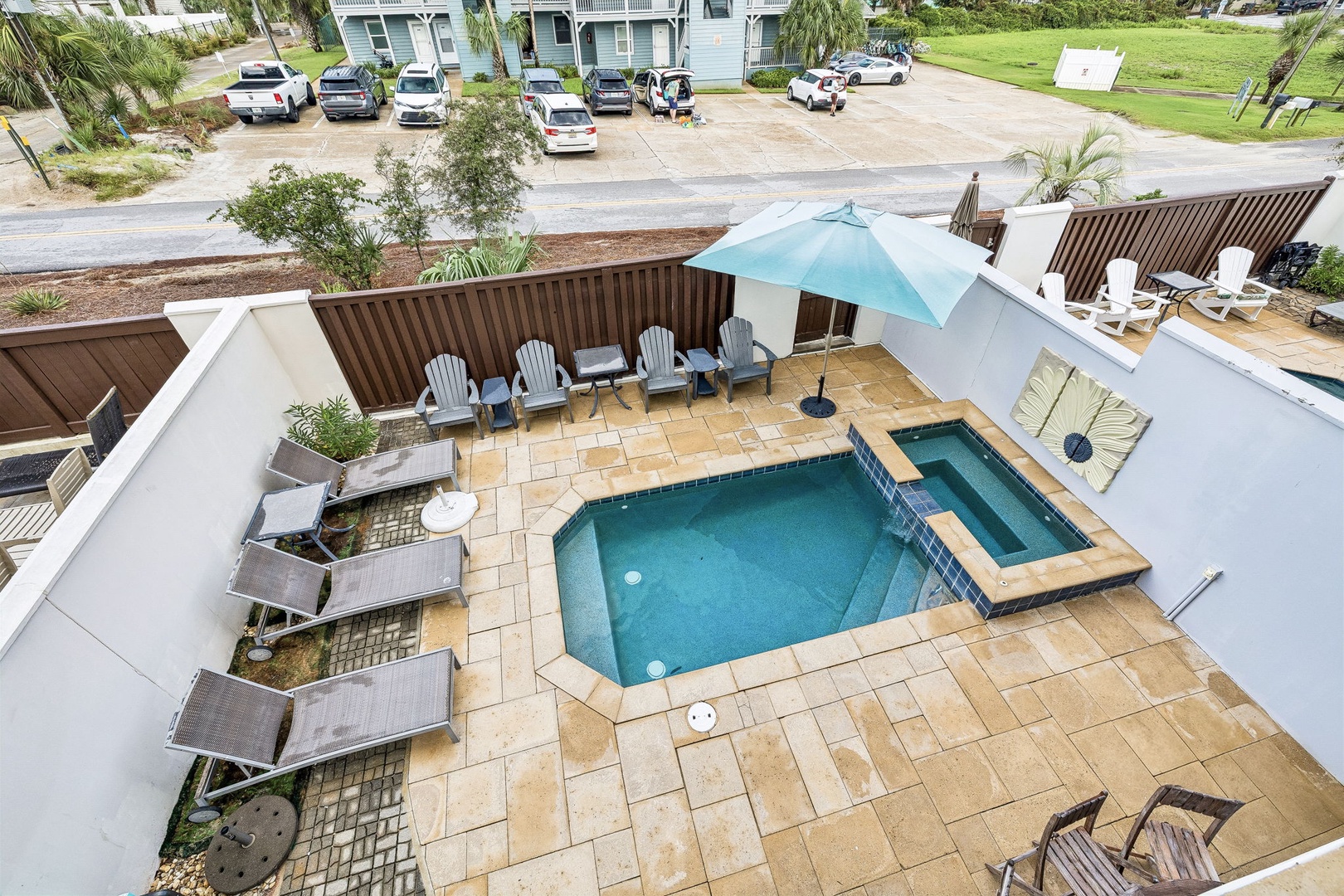 Aerial view of the property's private outdoor area featuring a swimming pool, hot tub, and patio seating within a landscaped, fenced yard with nearby parking.
