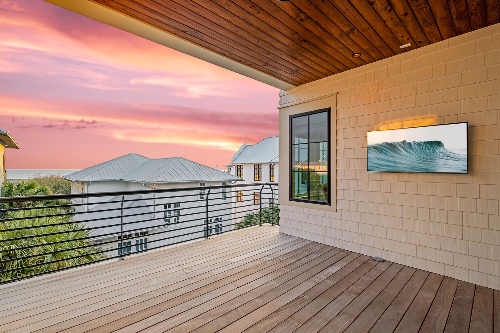 Covered balcony with modern outdoor TV viewing area and sunset sky over residential neighborhood.