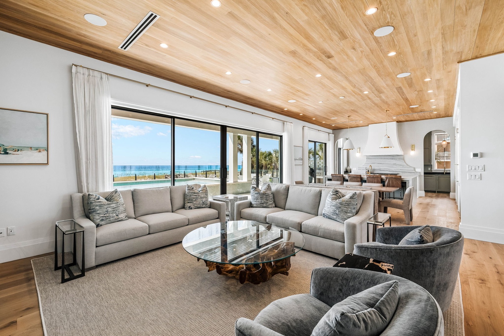 Relax in your stylish living room with expansive windows framing stunning ocean views. The warm wood ceiling, plush seating, and seamless flow to the pool and beach beyond create the perfect coastal escape.