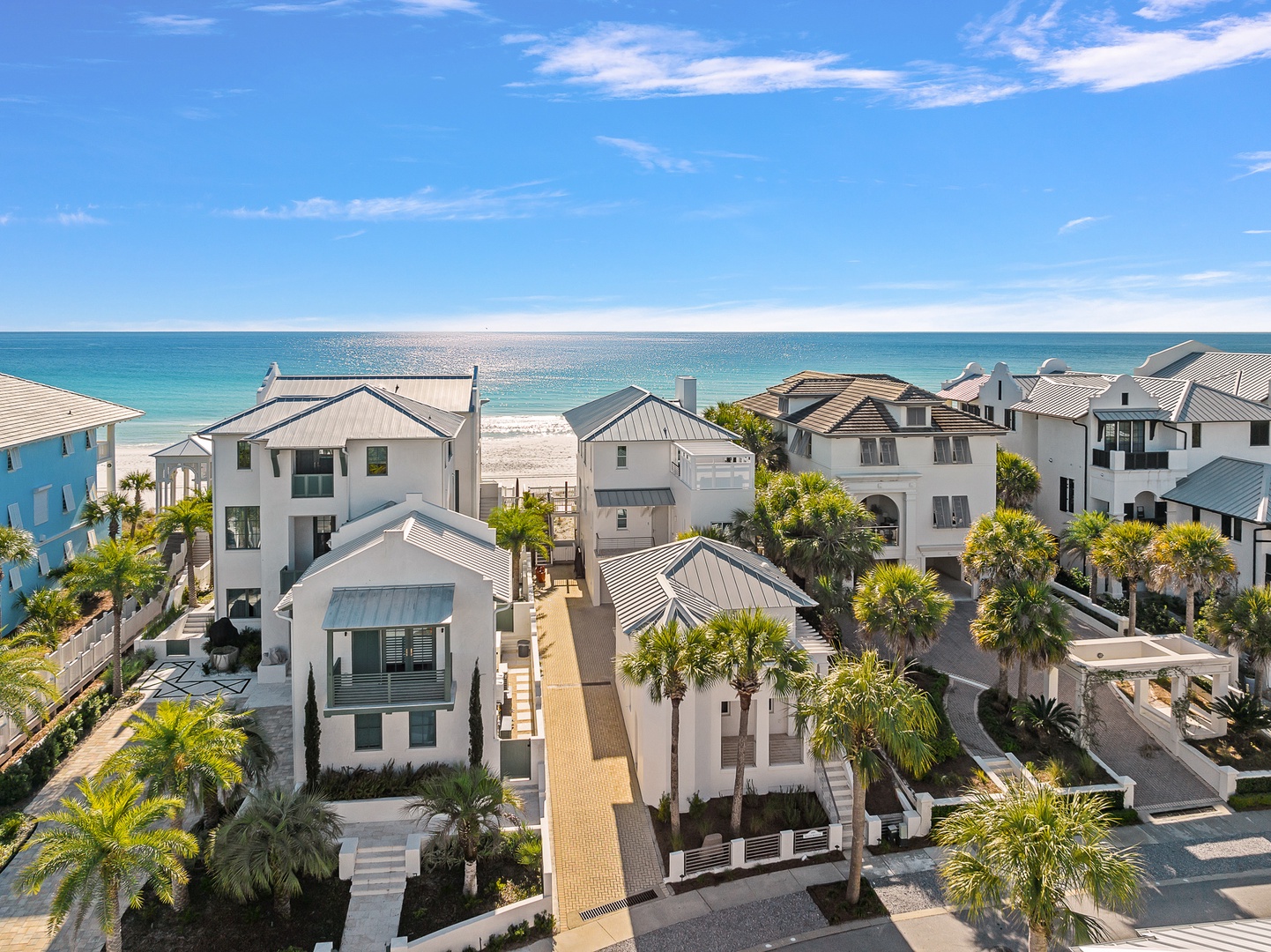 Stunning beachfront community featuring elegant coastal homes with palm trees and pristine white sand beach access.