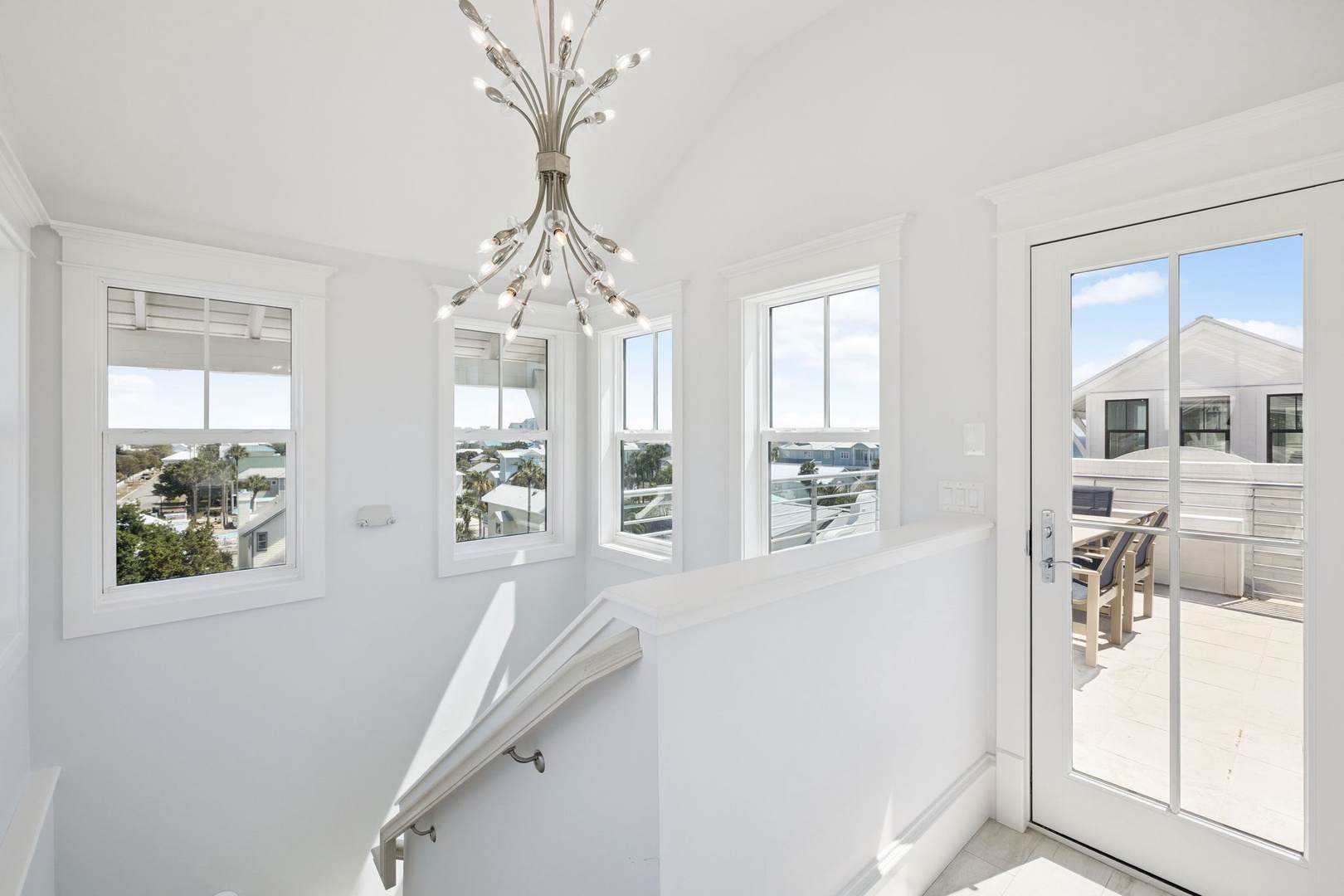 Bright coastal views fill your elegant space through floor-to-ceiling windows, while gleaming white interiors and stunning chandelier create pure luxury.