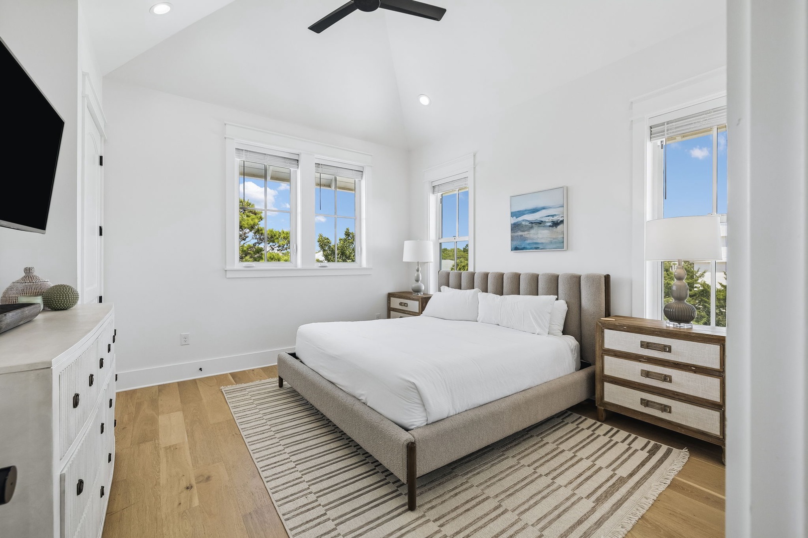 Your bright, airy retreat features a plush queen bed under vaulted ceilings, with natural light streaming through multiple windows. Coastal art and warm wood floors create a peaceful atmosphere for unwinding after your day's adventures.