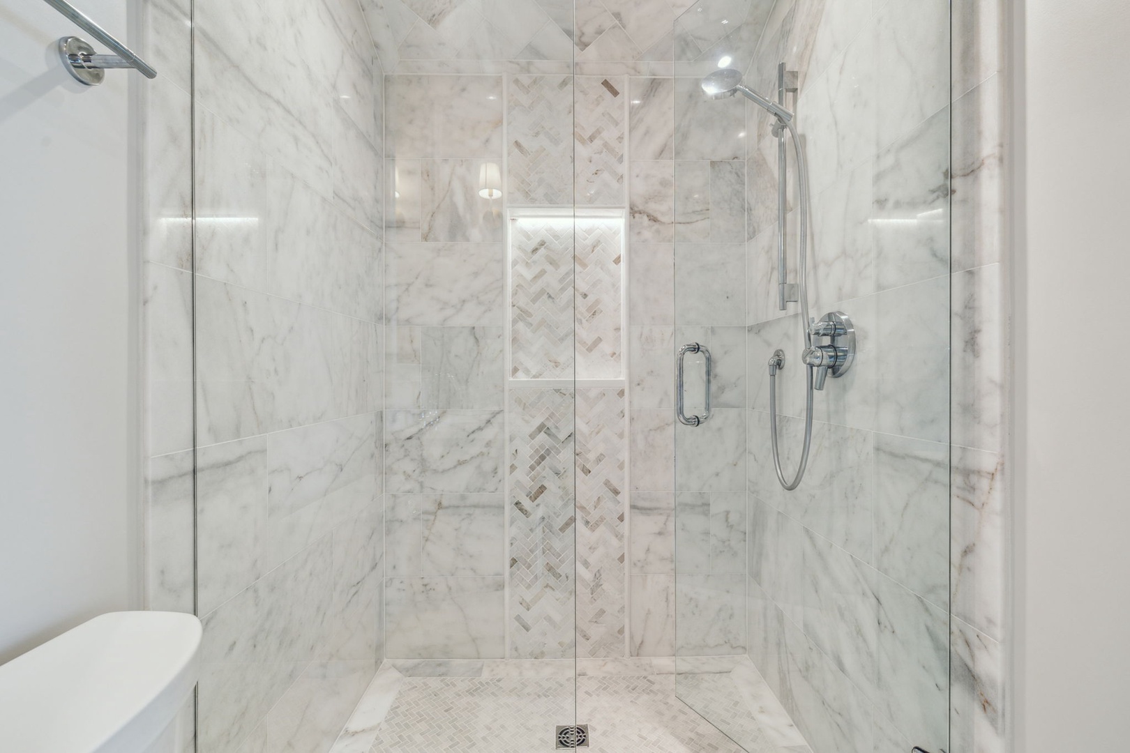 Luxurious marble walk-in shower with built-in shelving and dual fixtures. The elegant herringbone tile accent adds a sophisticated touch to your daily routine.