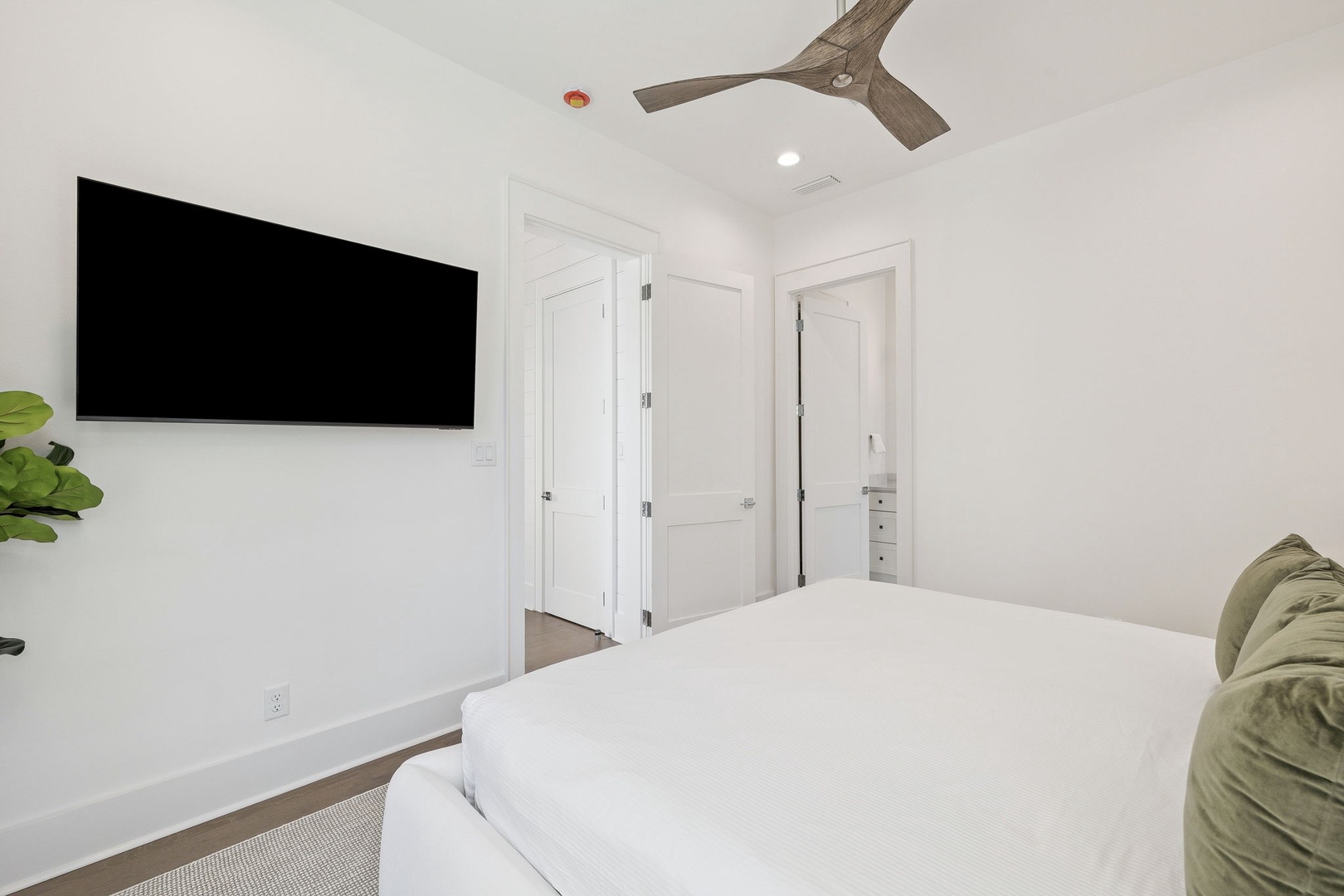 Unwind in your serene bedroom featuring crisp white linens, a large wall-mounted TV, and soothing natural light for ultimate relaxation.