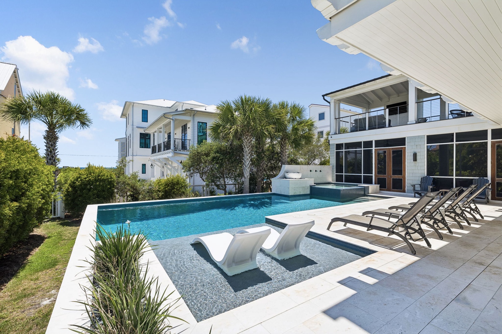 Modern coastal retreat features sparkling pool, hot tub, sun loungers, and tropical palms under sunny skies—a perfect spot for lounging and cooling off.