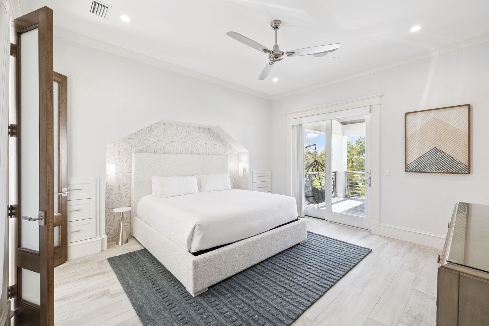 Relax in your serene bedroom featuring crisp white linens, gentle ceiling fan, and doors opening to your private outdoor space.