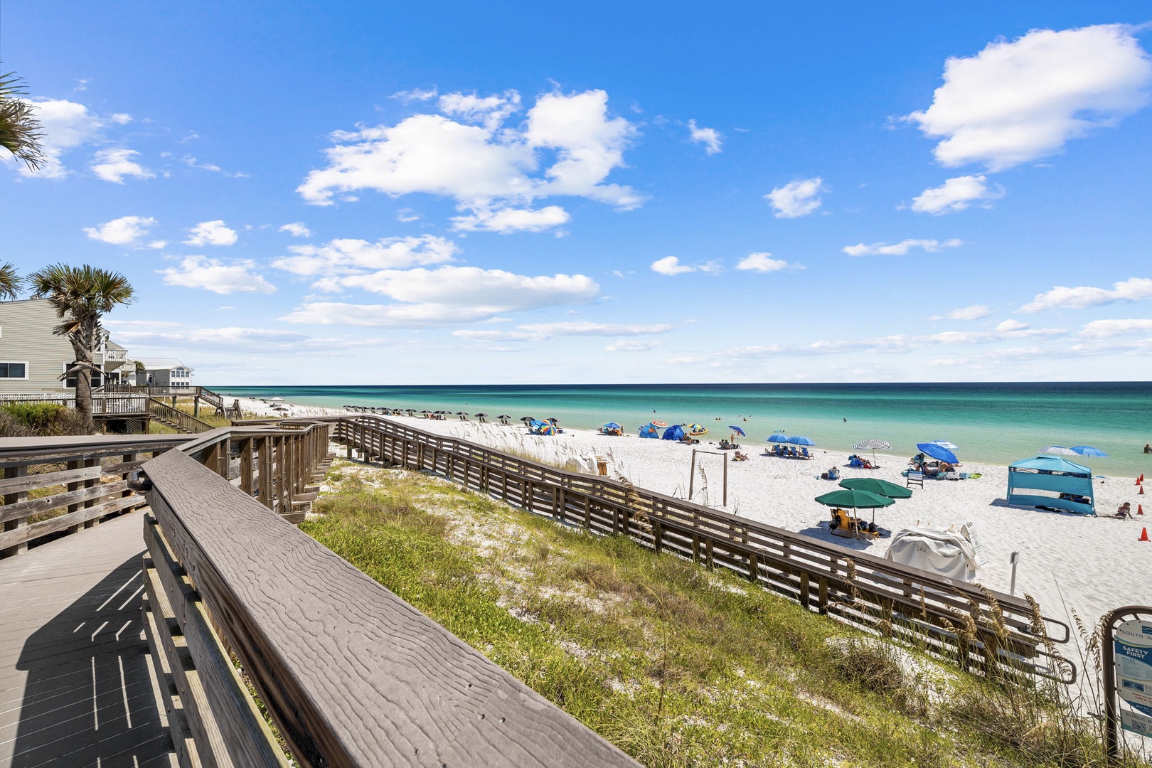 Pristine white sand beach with turquoise waters stretches along the Gulf Coast, featuring colorful umbrellas and beachgoers enjoying the perfect day.