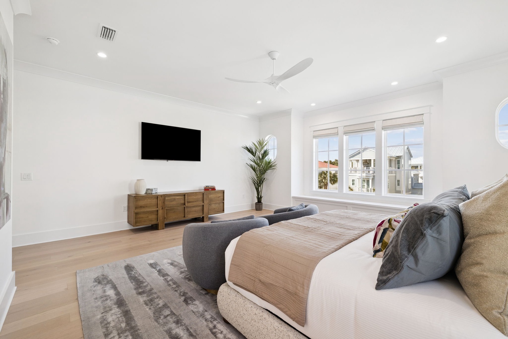 Unwind in your spacious bedroom featuring a plush king bed, wall-mounted TV, and bright windows showcasing neighborhood views.