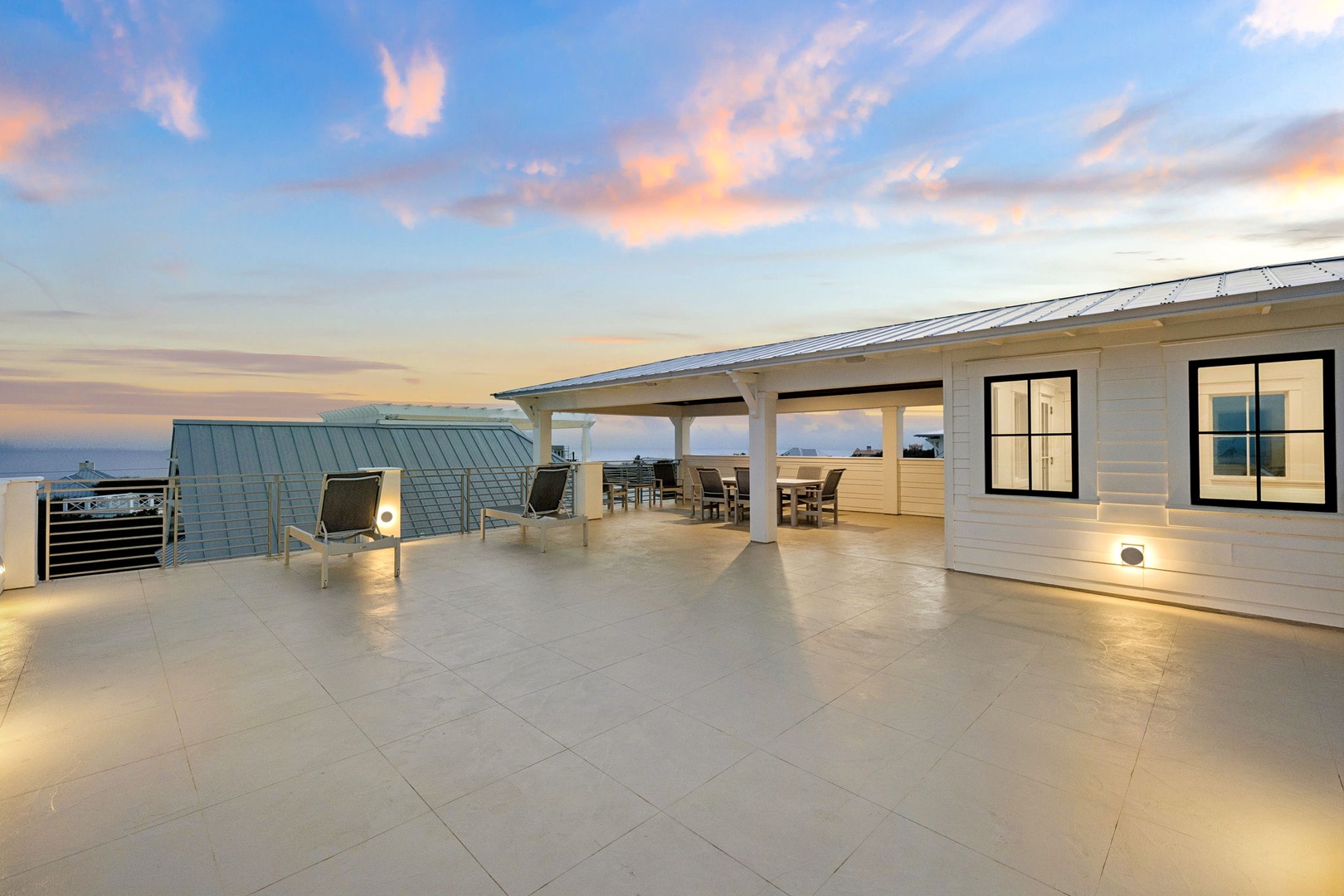 Expansive rooftop terrace features modern seating and dining areas beneath a dramatic sunset sky with panoramic views.