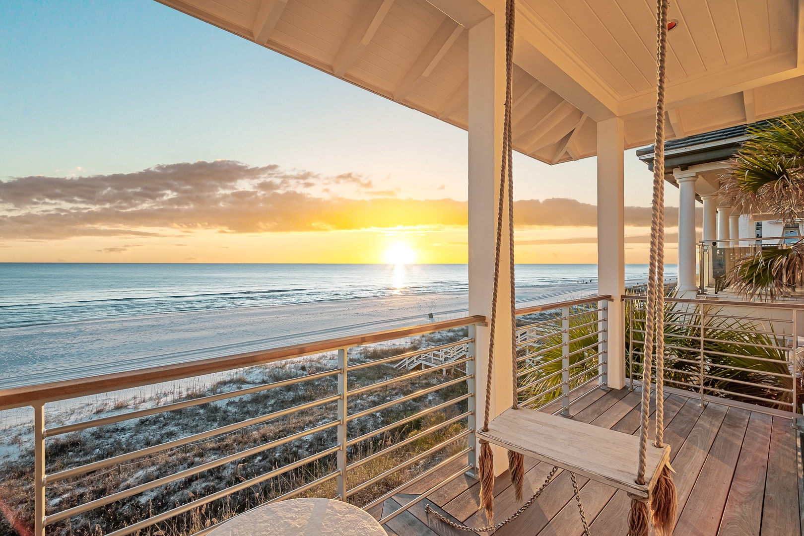 Beachfront deck with rope swing overlooks pristine sand and gentle waves, offering stunning sunset views from this coastal retreat.