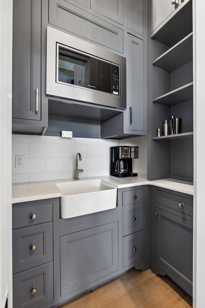 Your own kitchenette awaits with everything you need: sparkling farmhouse sink, built-in microwave, coffee maker, and generous shelving for your pantry favorites. Sleek gray cabinetry and white subway tile add modern charm to your stay.