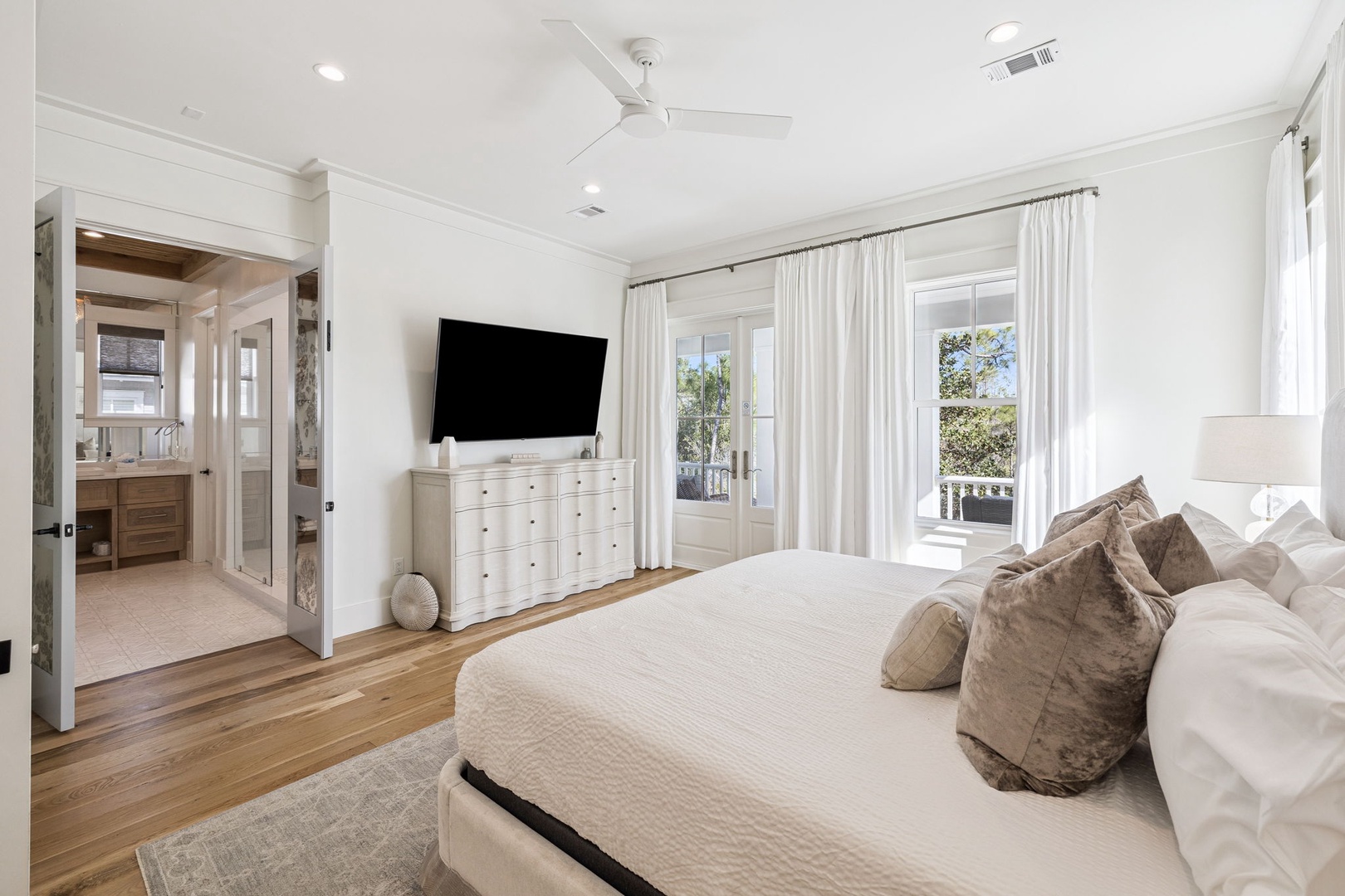 Unwind in your serene master bedroom with plush bedding, TV entertainment, and sunlight streaming through elegant windows.