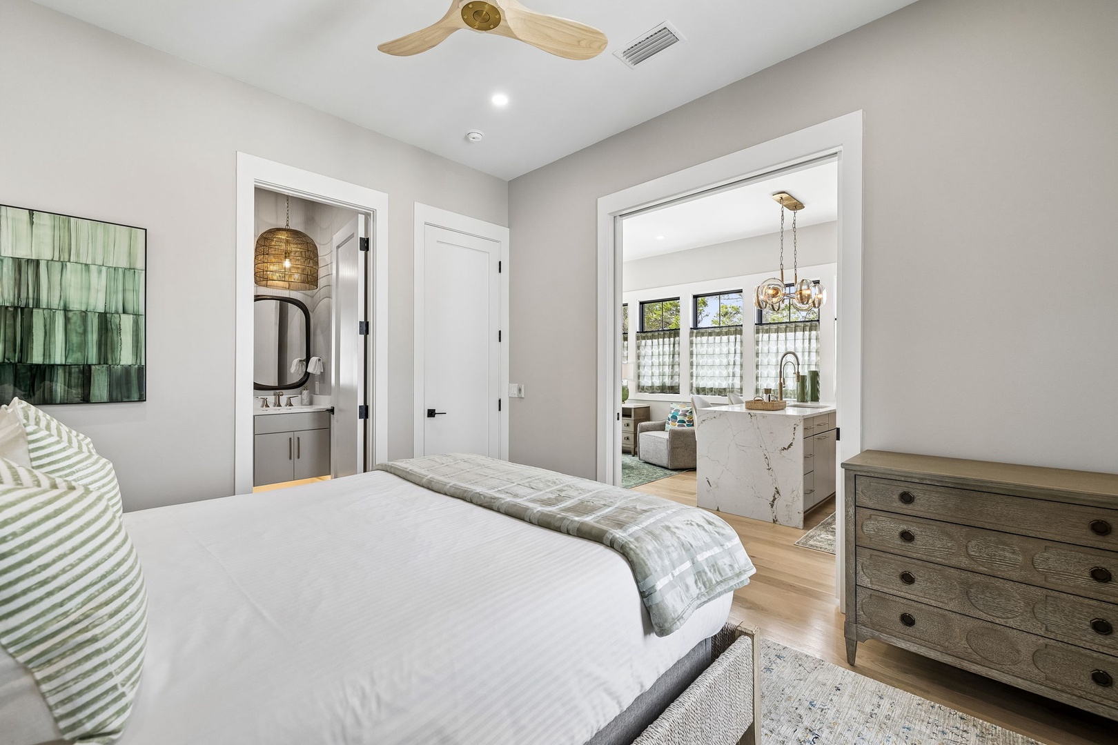 Unwind in your serene bedroom with plush bedding, stylish furnishings, and en-suite bath. Natural light flows through to the open kitchen beyond, creating a bright and inviting retreat.