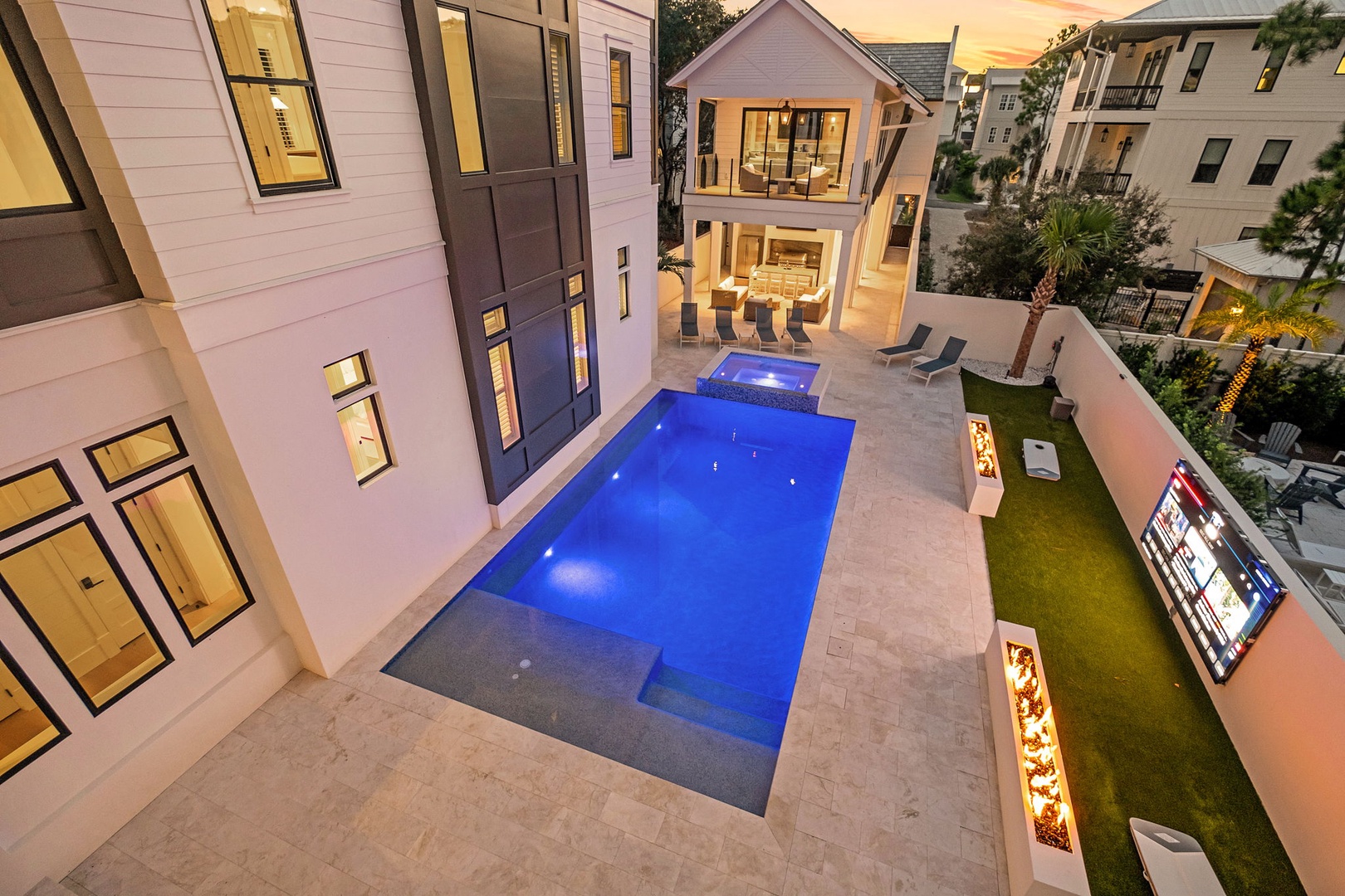 Aerial view of a luxury vacation home showcasing its pool, courtyard, and contemporary architecture set within a vibrant coastal neighborhood.