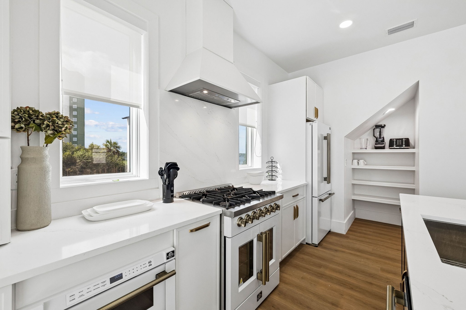 Step into a bright, modern kitchen with sleek white cabinetry, a professional-style range, and warm wood flooring that makes cooking feel effortless.