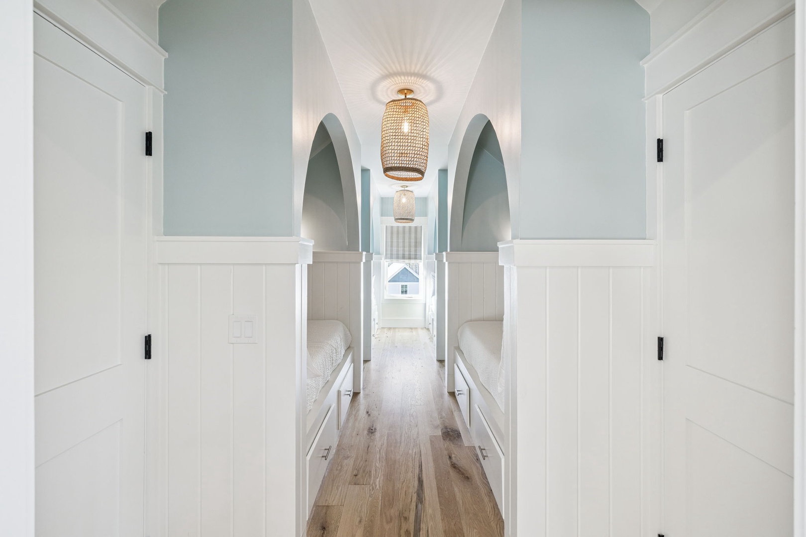 Your charming bunk room awaits with built-in beds, elegant archways, and warm wicker lighting creating a cozy coastal retreat.