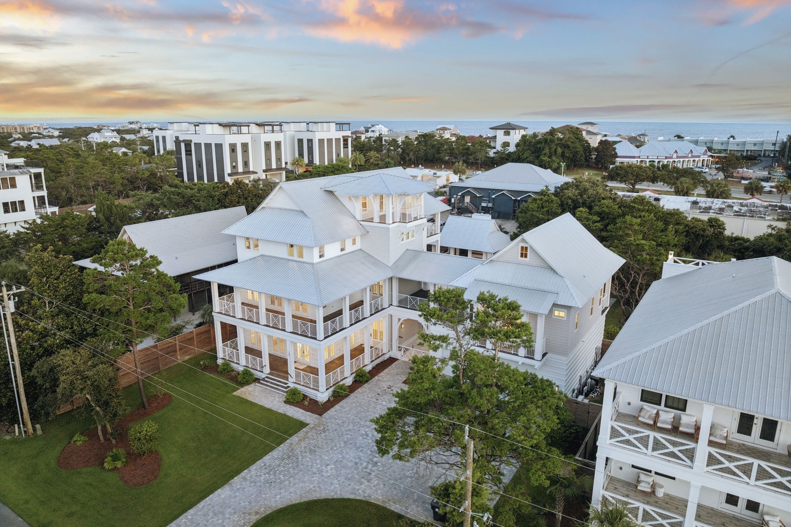 An impressive coastal estate surrounded by lush trees and neighboring properties, situated near the waterfront in a serene residential area.