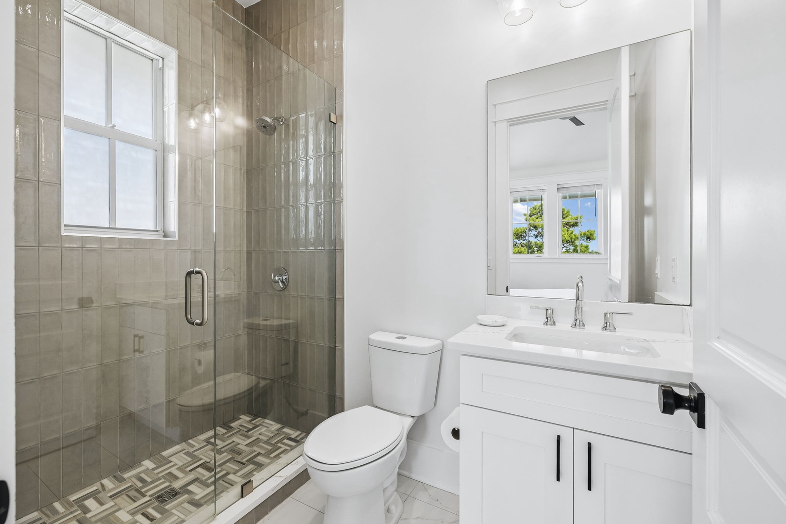 A pristine bathroom where your day begins with style. Fresh, bright, and beautifully designed with elegant tile work, a walk-in shower, and a peaceful view framed by the window.