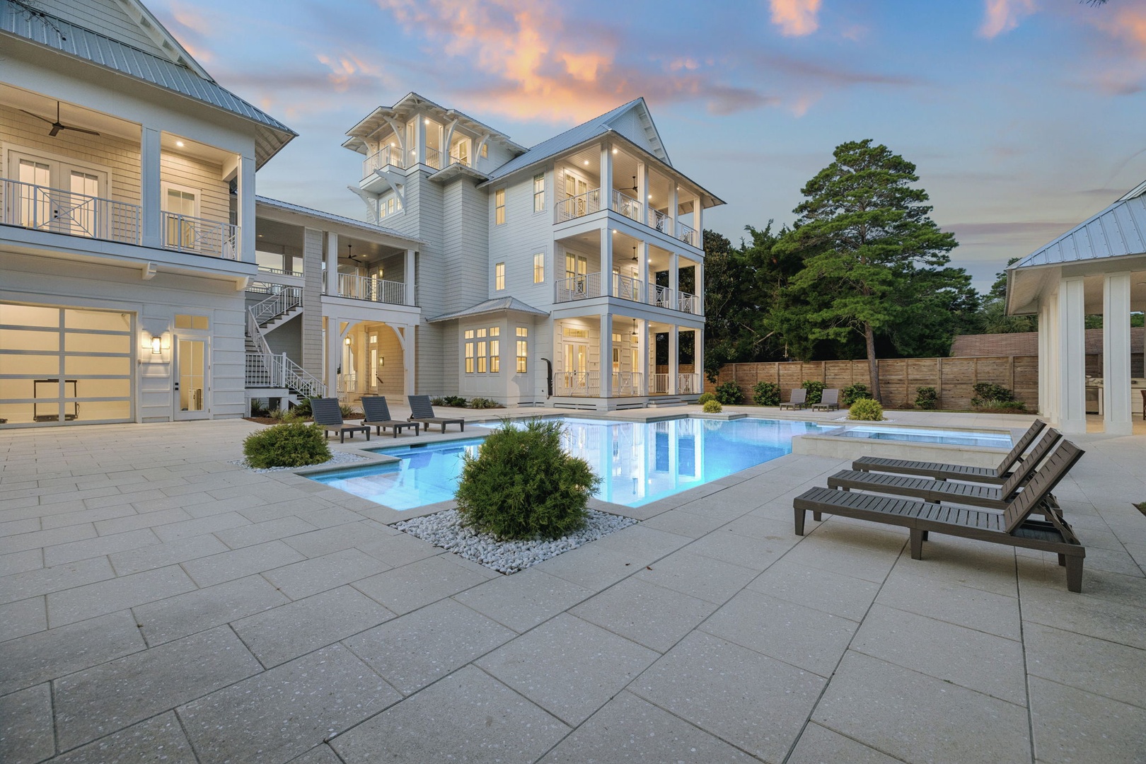 This elegant coastal estate features a stunning outdoor pool framed by lush landscaping, perfect for soaking up the sun on spacious loungers as twilight paints the sky in warm hues.