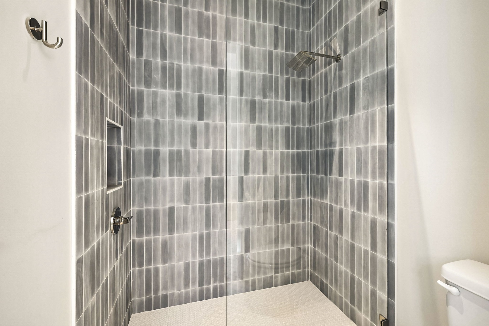 Your private glass-enclosed walk-in shower features elegant gray vertical tiling, a modern rainfall showerhead, and sleek fixtures for a refreshing, spa-like experience.