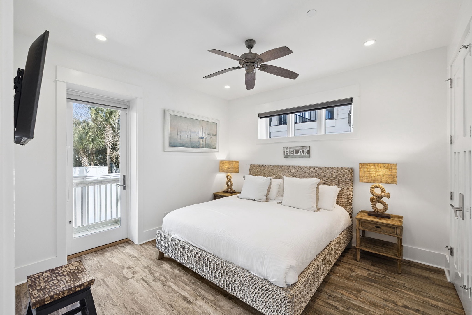 Drift off in this peaceful bedroom featuring coastal charm with wicker details, warm lighting, and a ceiling fan for your comfort.