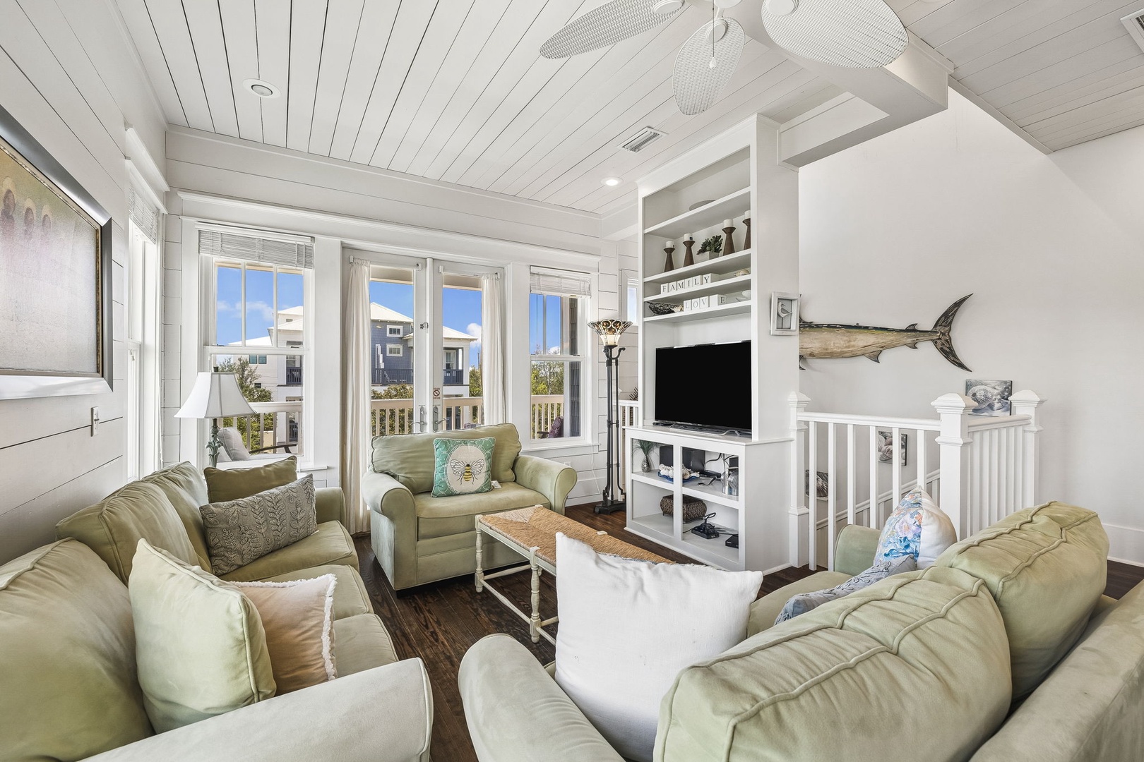 Settle into your coastal sanctuary where soft sage sofas invite you to unwind. Large windows frame bright skies and breezy views, while natural wood accents and beach-inspired touches create a relaxed, welcoming vibe.
