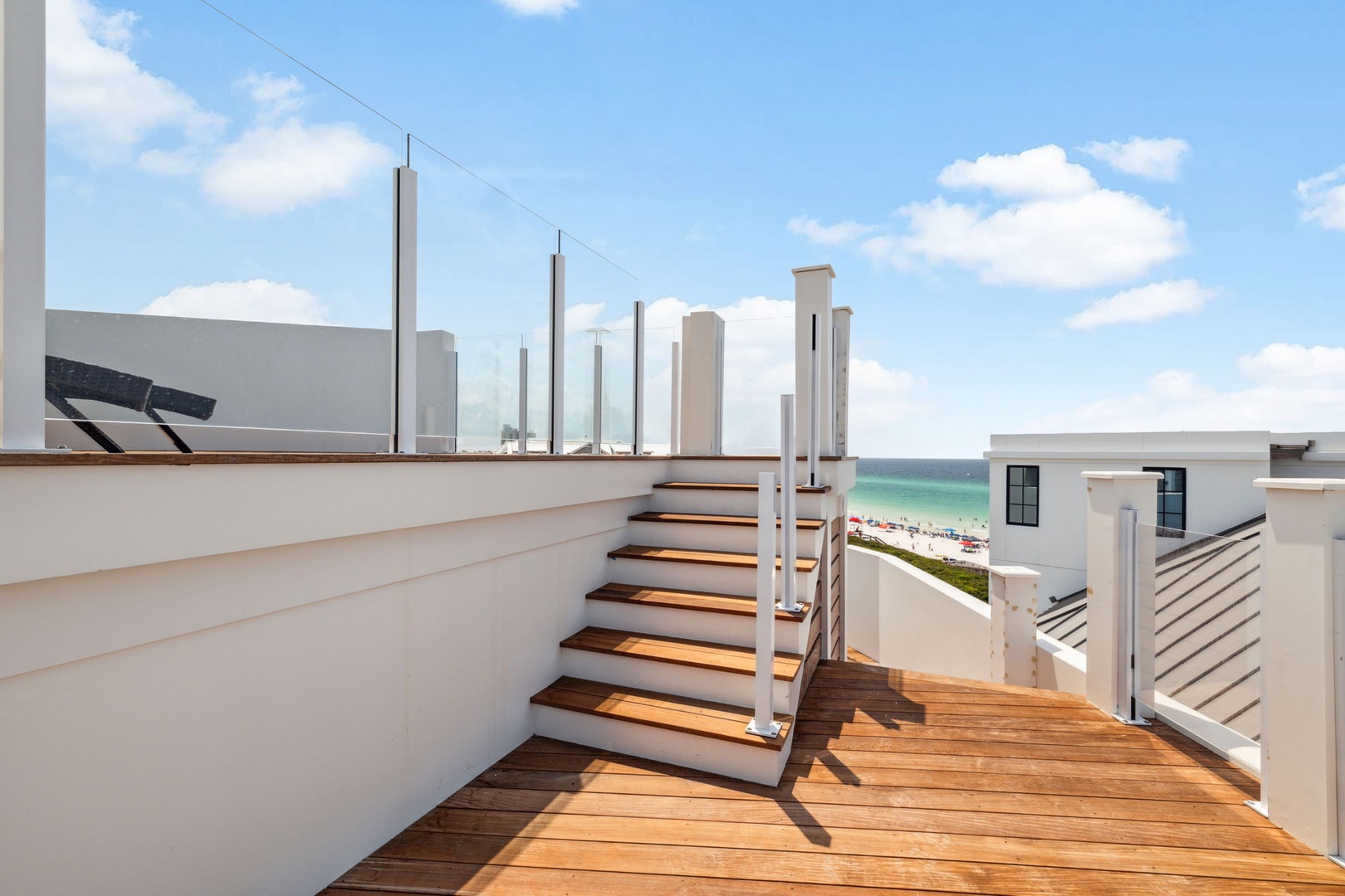 A modern rooftop deck with stunning ocean views stretches before you, offering warm wooden steps and pristine railings. This private outdoor space overlooks the turquoise water and sandy beach.