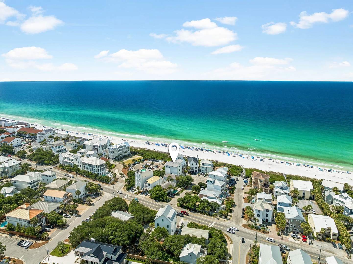 Aerial view captures a pristine coastal community with white-sand beaches meeting emerald Gulf waters, surrounded by charming beach houses and coastal architecture.