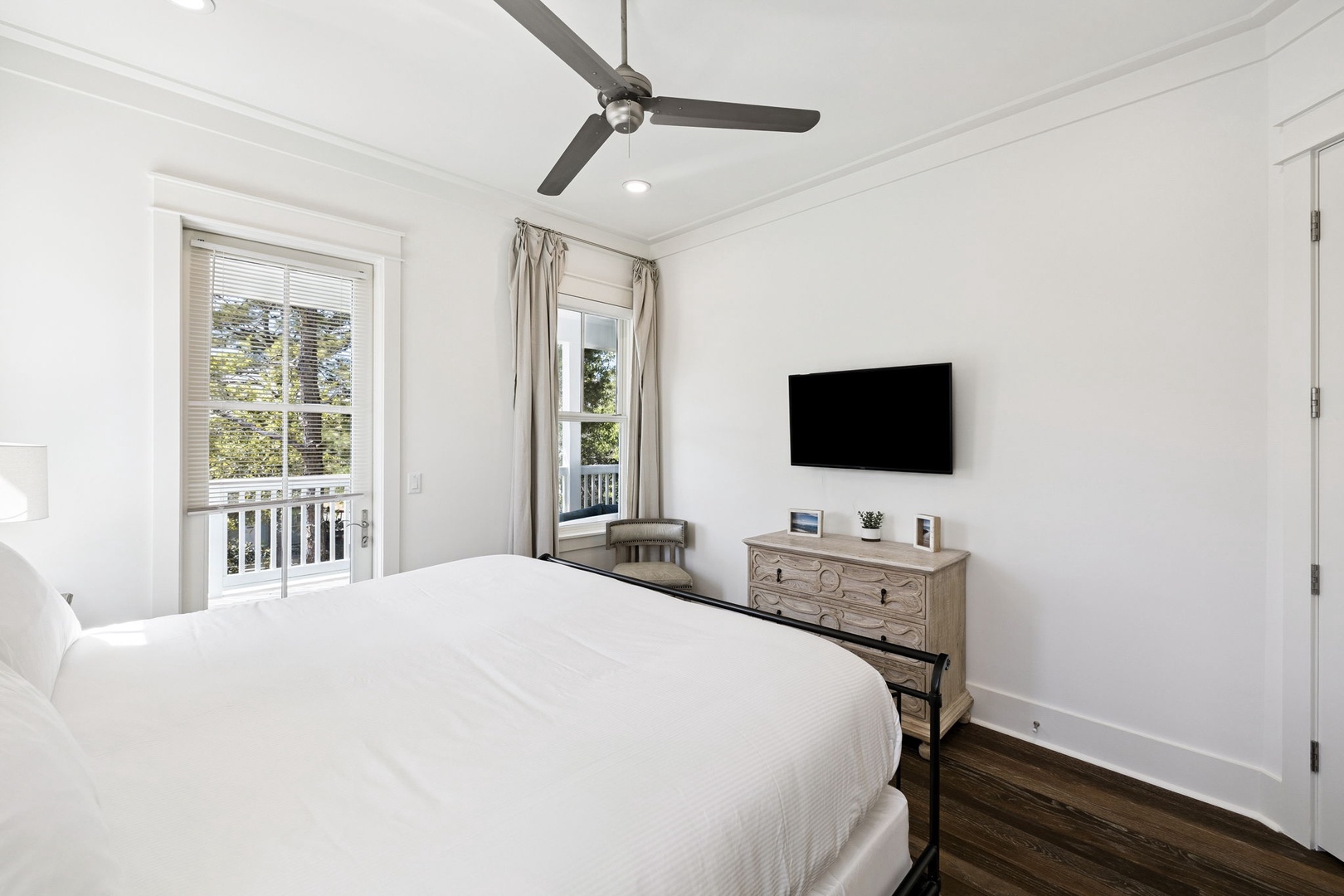 Drift into peaceful sleep in your bright bedroom featuring crisp white linens, modern TV, and balcony access to fresh air.