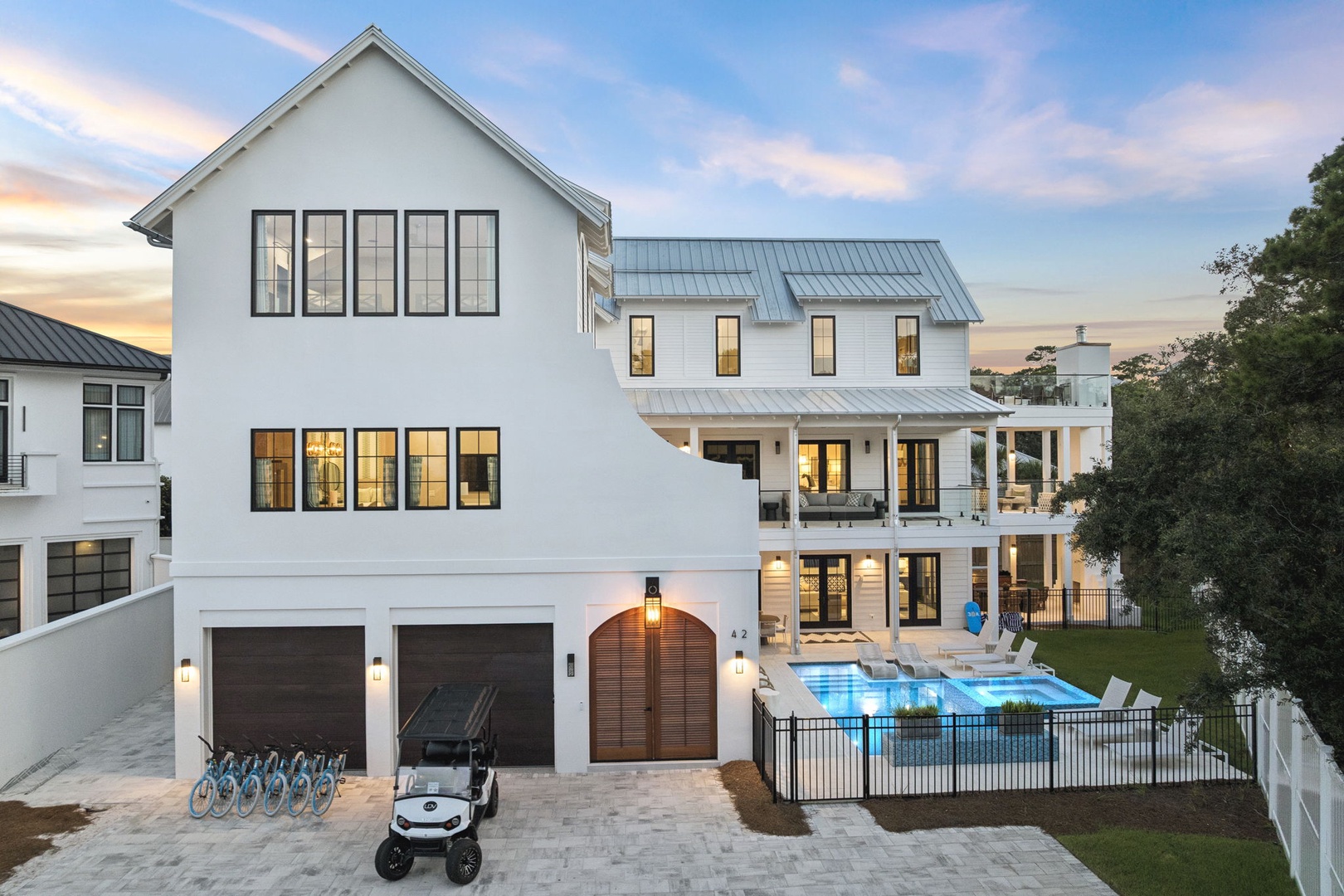 A modern coastal home with clean white architecture and metal roofing, featuring multiple levels and a sparkling pool surrounded by loungers in the landscaped yard.