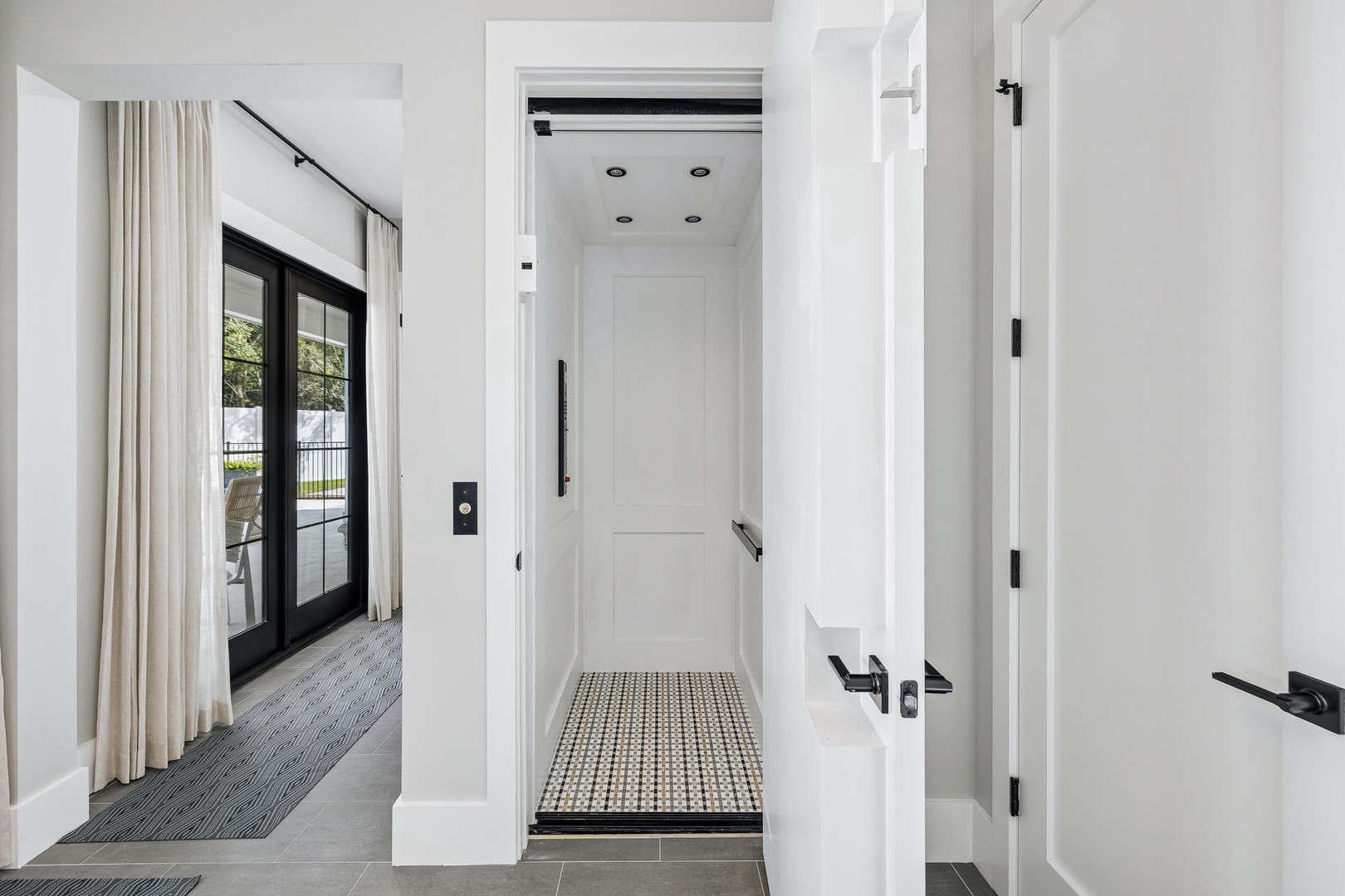 Modern convenience meets clean design. Your private elevator ensures easy access to all floors, complemented by sleek black hardware and bright natural light streaming through glass doors.