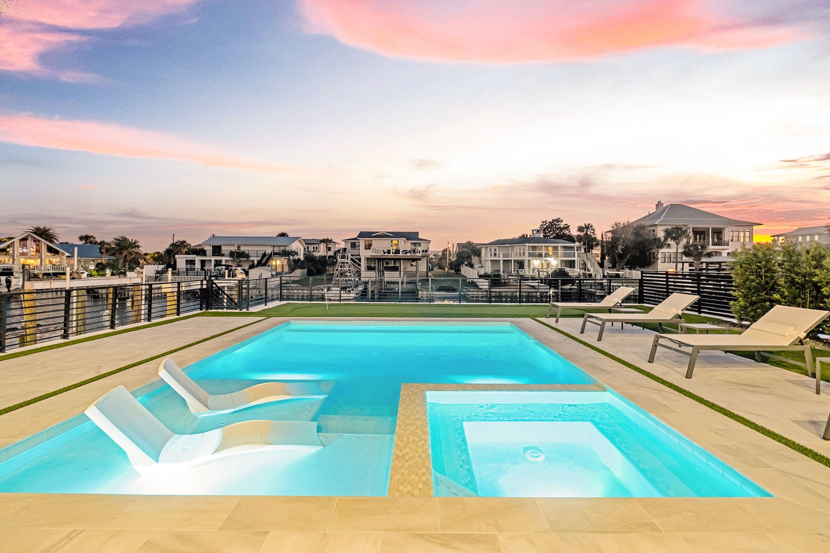 Stunning multi-level pool with spa under a painted sunset sky, surrounded by modern coastal homes in this exclusive waterfront neighborhood.