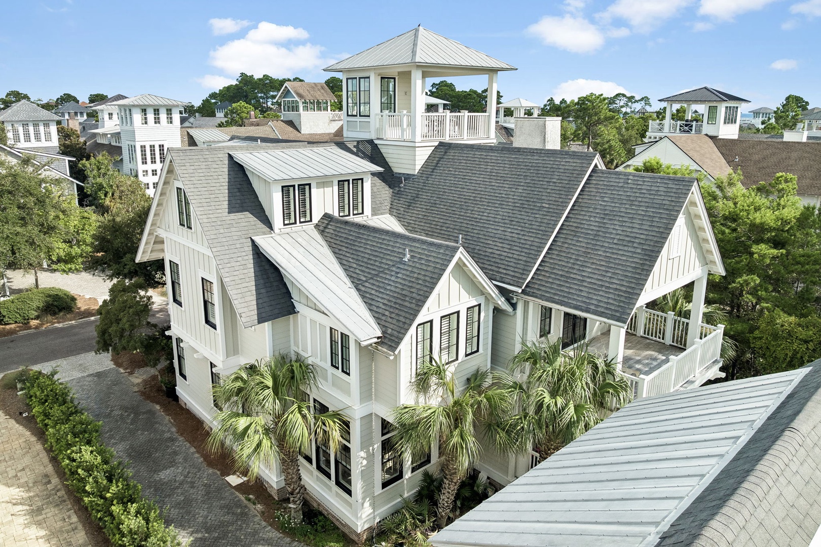 A stunning coastal home nestled in a charming neighborhood, featuring elegant rooftop architecture with a viewing tower, surrounded by lush palm trees and mature landscaping.