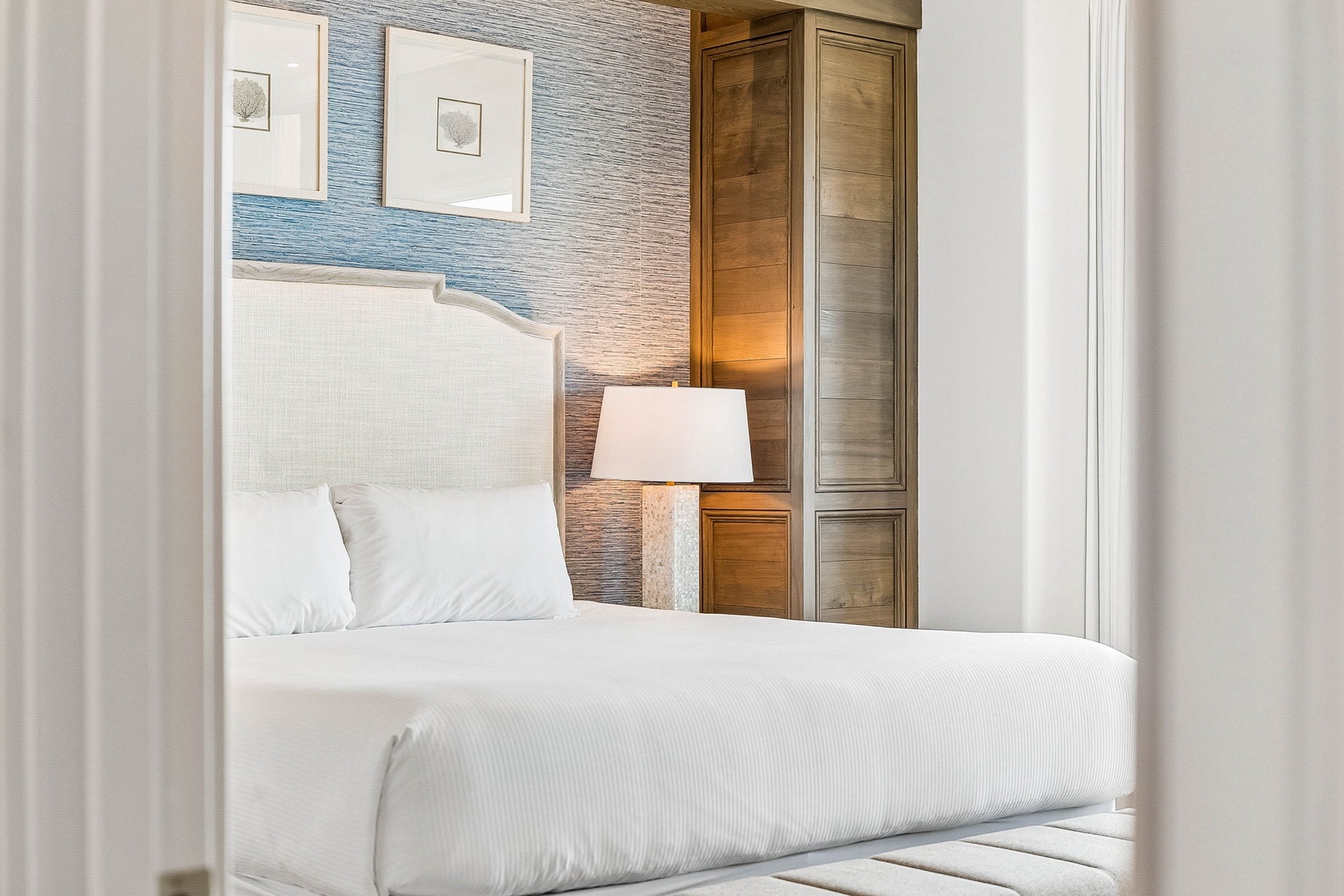Slip into crisp white linens and unwind in your serene coastal retreat, where soft textures, soothing blue accent walls, and warm bedside lighting create the perfect escape.