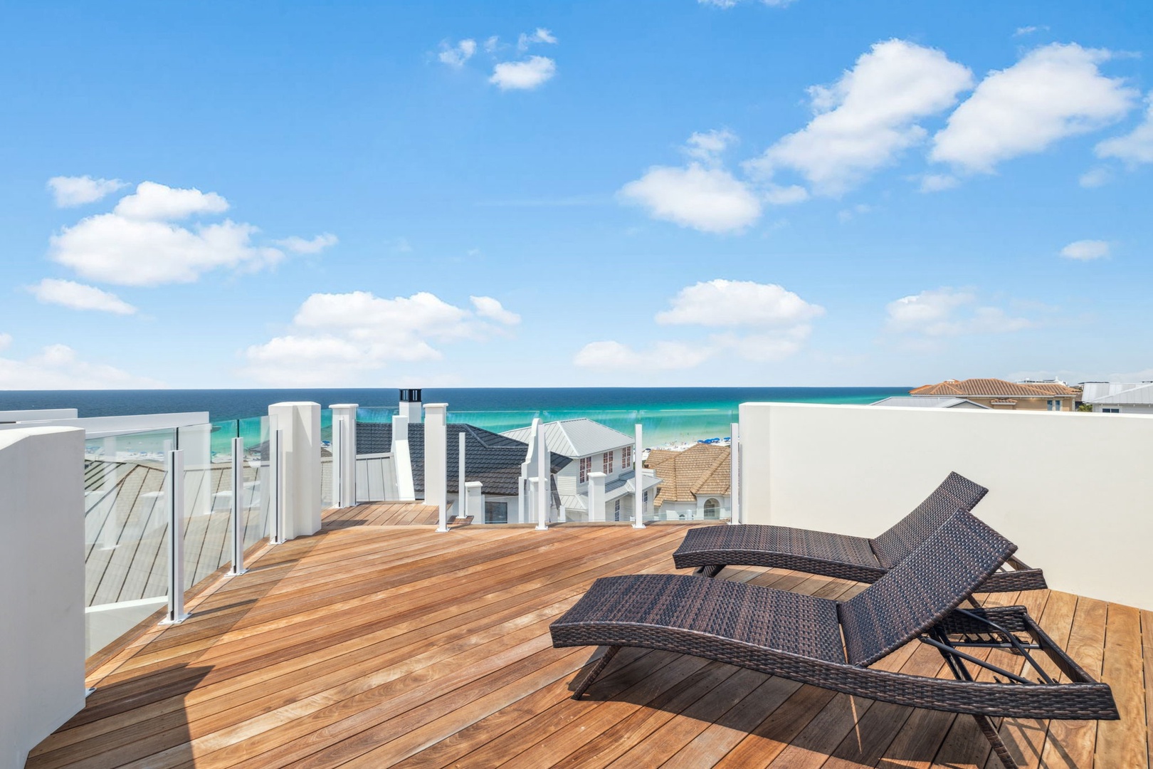 Rooftop terrace overlooking coastal neighborhoods and the stunning turquoise ocean beyond, framed by a bright blue sky and scattered clouds.