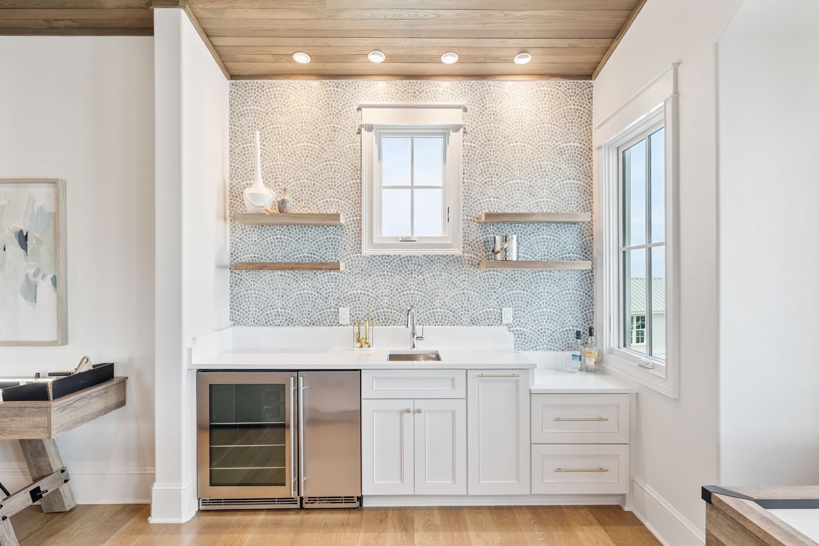 Prepare your favorite drinks at this elegant wet bar, featuring a stylish mosaic backsplash, open wood shelving, a beverage cooler, and gleaming countertops—perfect for entertaining in style.