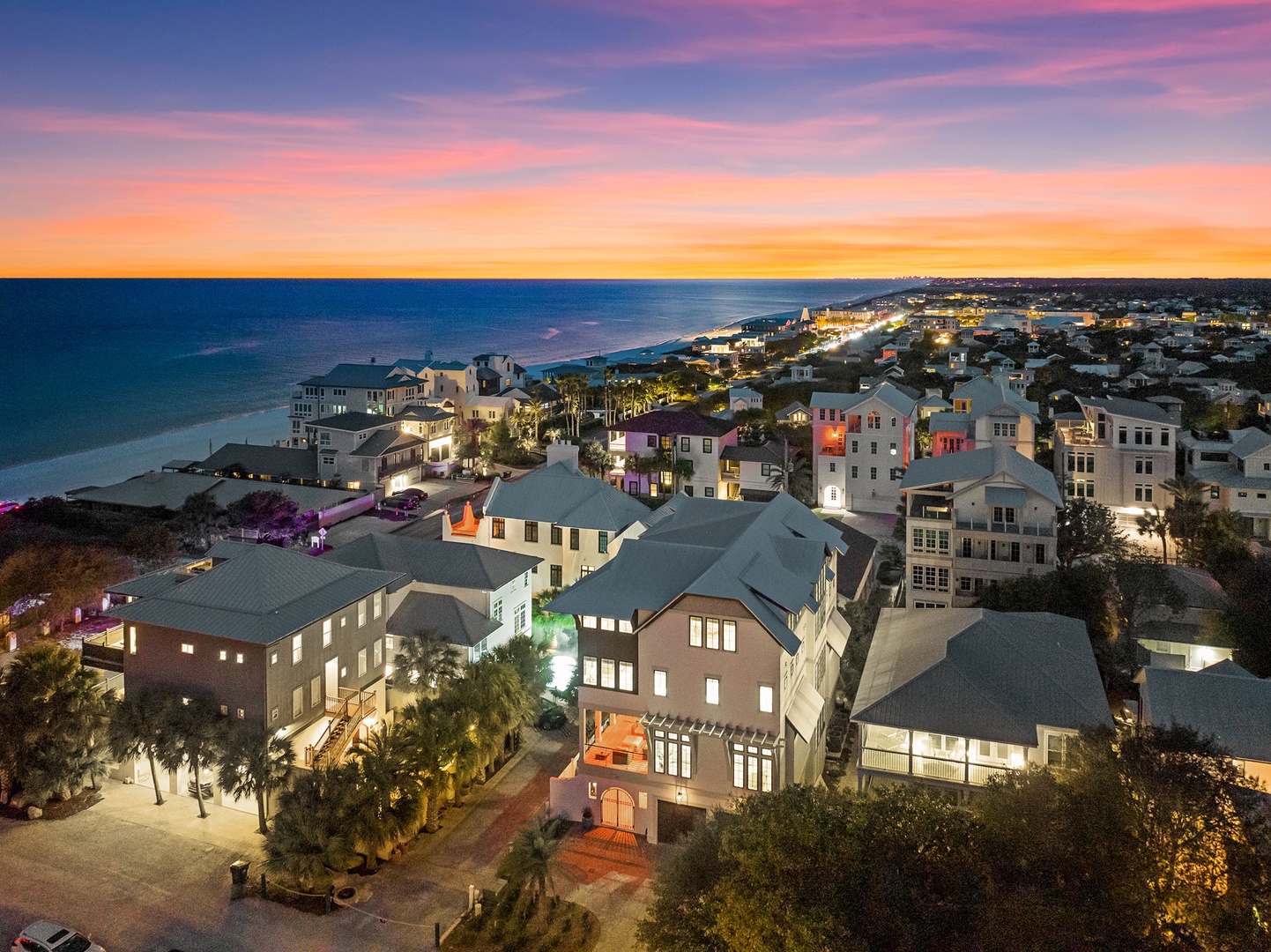 Spectacular sunset paints the sky over this charming beachfront community, showcasing colorful coastal homes and pristine sandy shores.