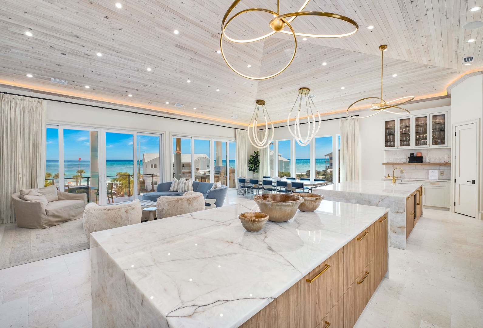 Sunlight streams through floor-to-ceiling windows, framing stunning ocean views from your spacious kitchen and living area. Gold fixtures and natural wood add warmth to the elegant marble surfaces where you'll gather.