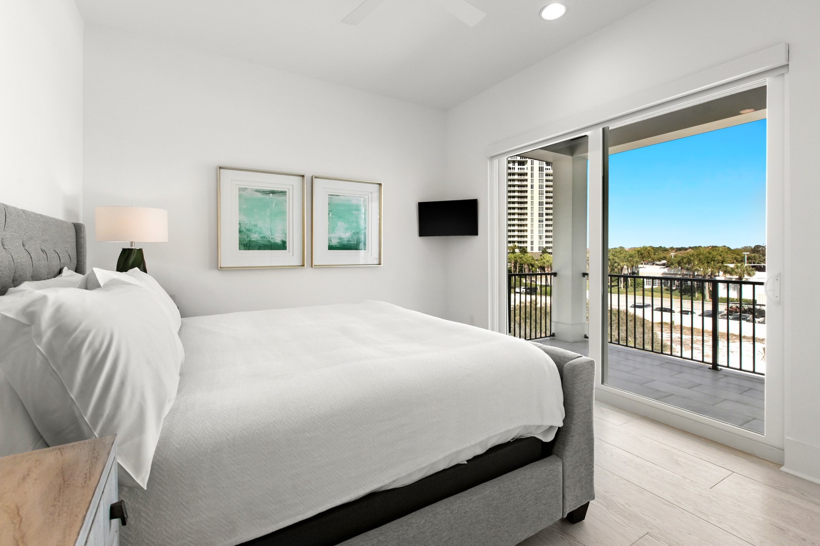 Wake up to bright skies and city views from your private balcony. This serene bedroom invites you to unwind in crisp linens and soothing coastal tones.