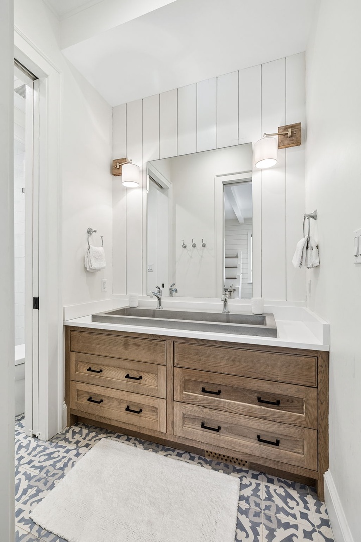 Step into your modern farmhouse bathroom with its sleek double vanity, charming wood accents, and elegant patterned tile. The white shiplap walls and warm lighting create a fresh, inviting space for your morning routine.