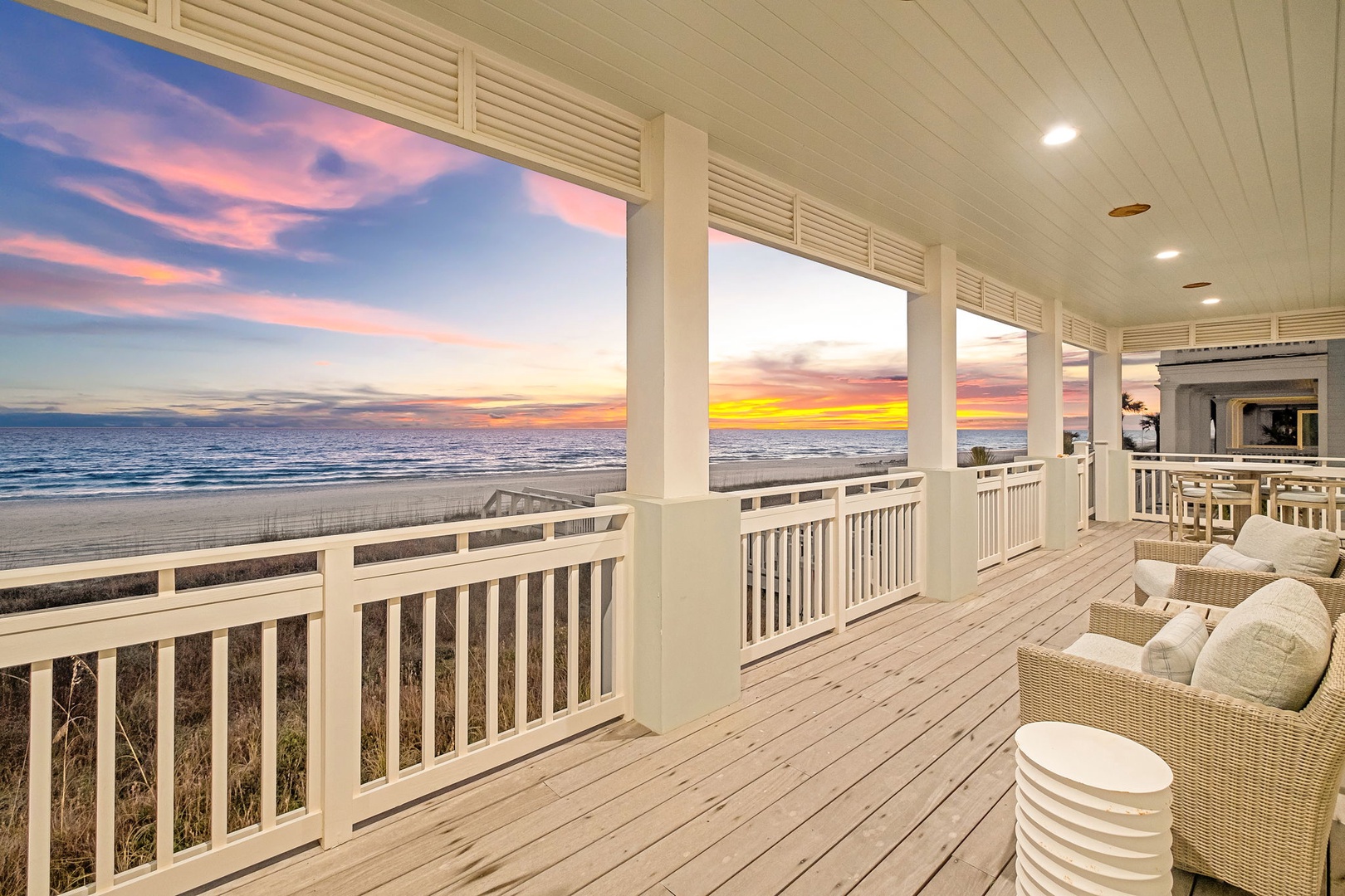 Expansive beachfront deck showcases breathtaking sunset views over the ocean, featuring coastal-style seating for relaxation. This elegant outdoor space offers a perfect vantage point for the natural beauty of the surrounding beachfront area.