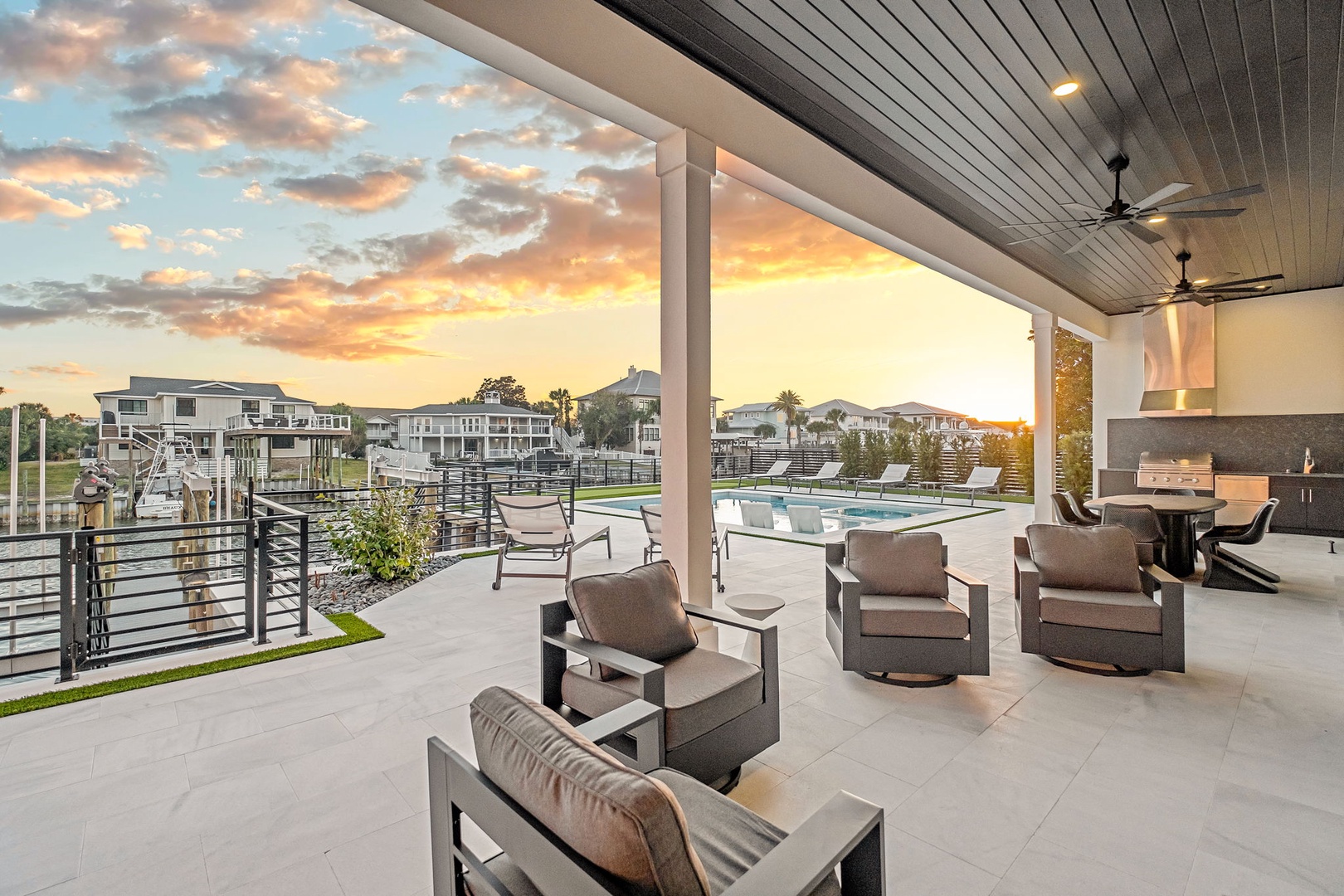 Unwind in this stunning covered terrace featuring a dramatic sunset backdrop and modern lakefront community views.