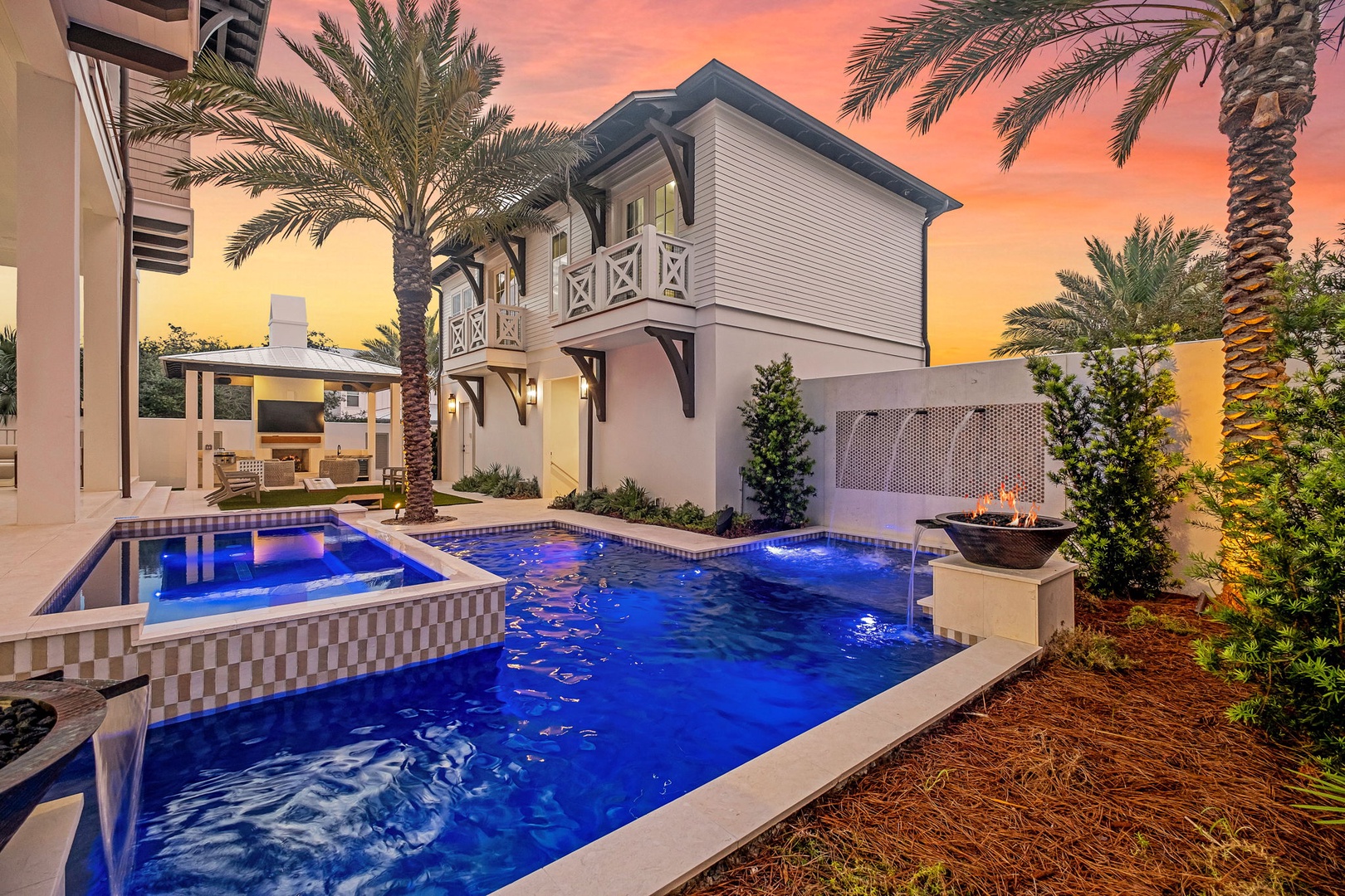 A stunning poolside retreat framed by palm trees at dusk, with a hot tub and fire feature completing the serene tropical setting. Perfect for unwinding under painted skies.