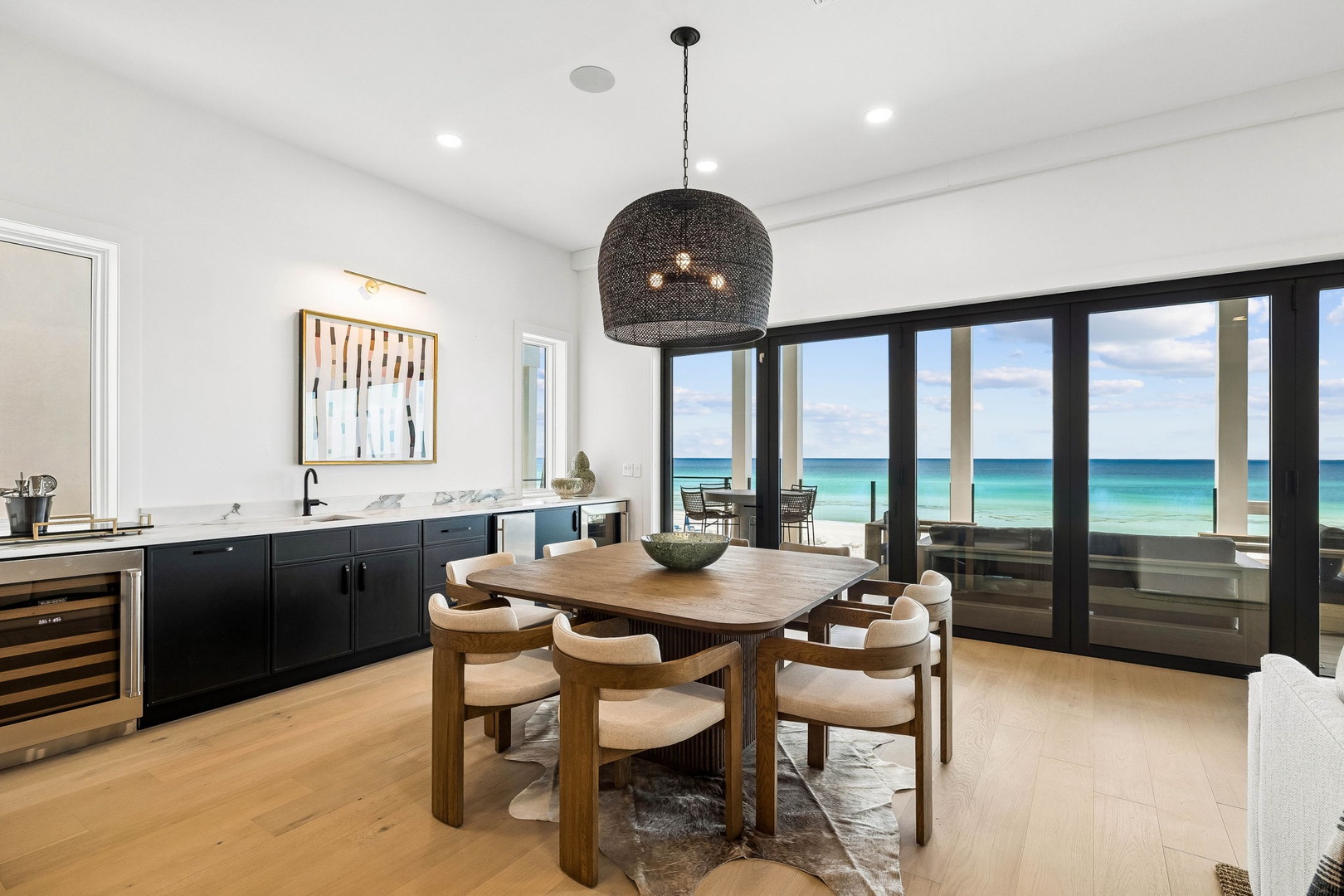 Step into your bright, open dining space where the ocean becomes your backdrop. Floor-to-ceiling windows frame endless turquoise waters, filling the room with natural light and coastal calm.