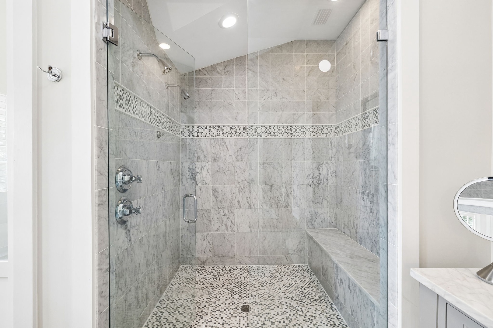 Step into your spa-like walk-in shower featuring elegant marble-style tilework, a built-in bench for comfort, and dual showerheads to rinse away the day in style.