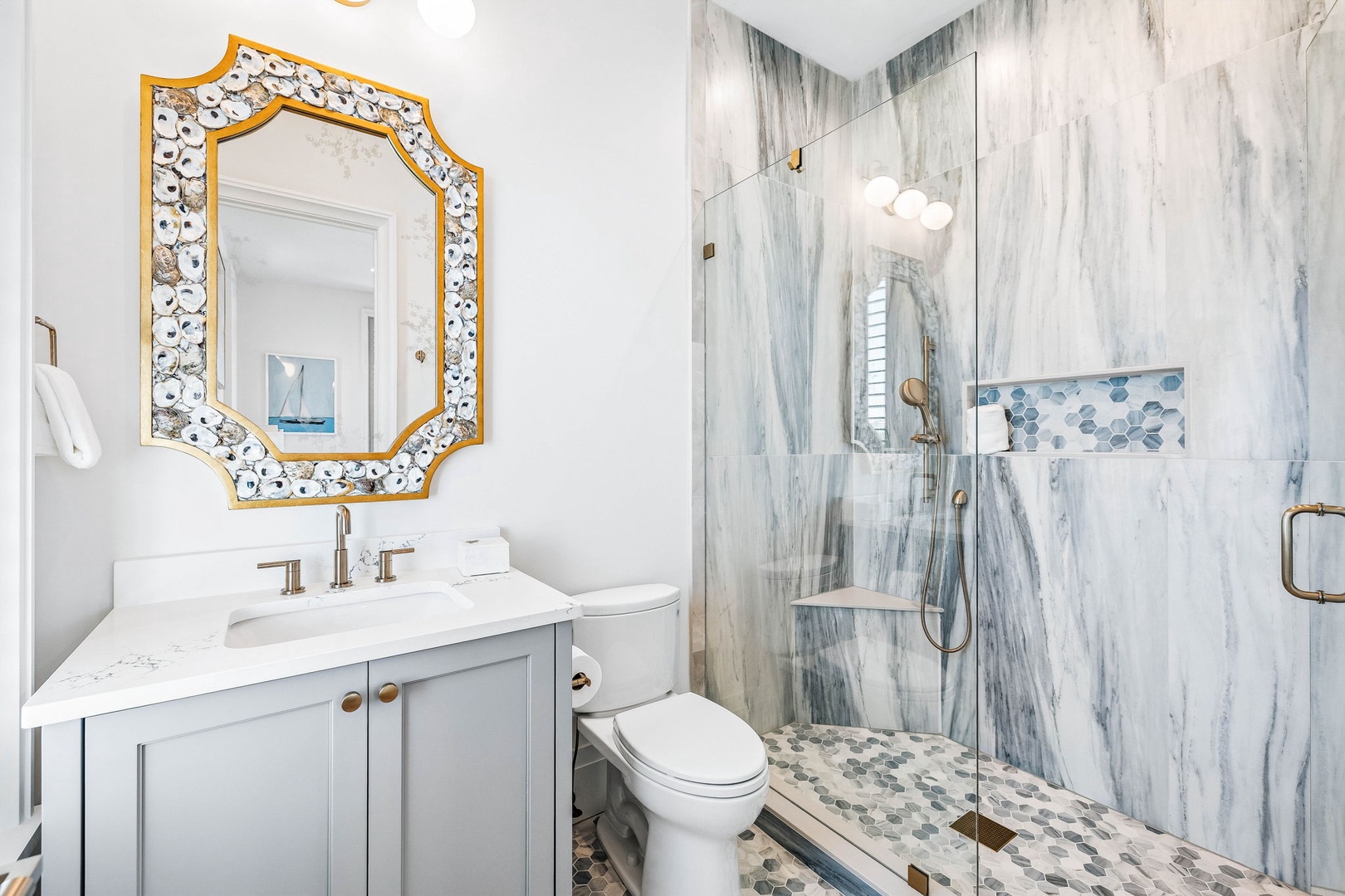 Elegant bathroom with marble-look walk-in shower, hexagonal mosaic accent, white quartz vanity, and gold-framed mirror creating a bright, sophisticated retreat.