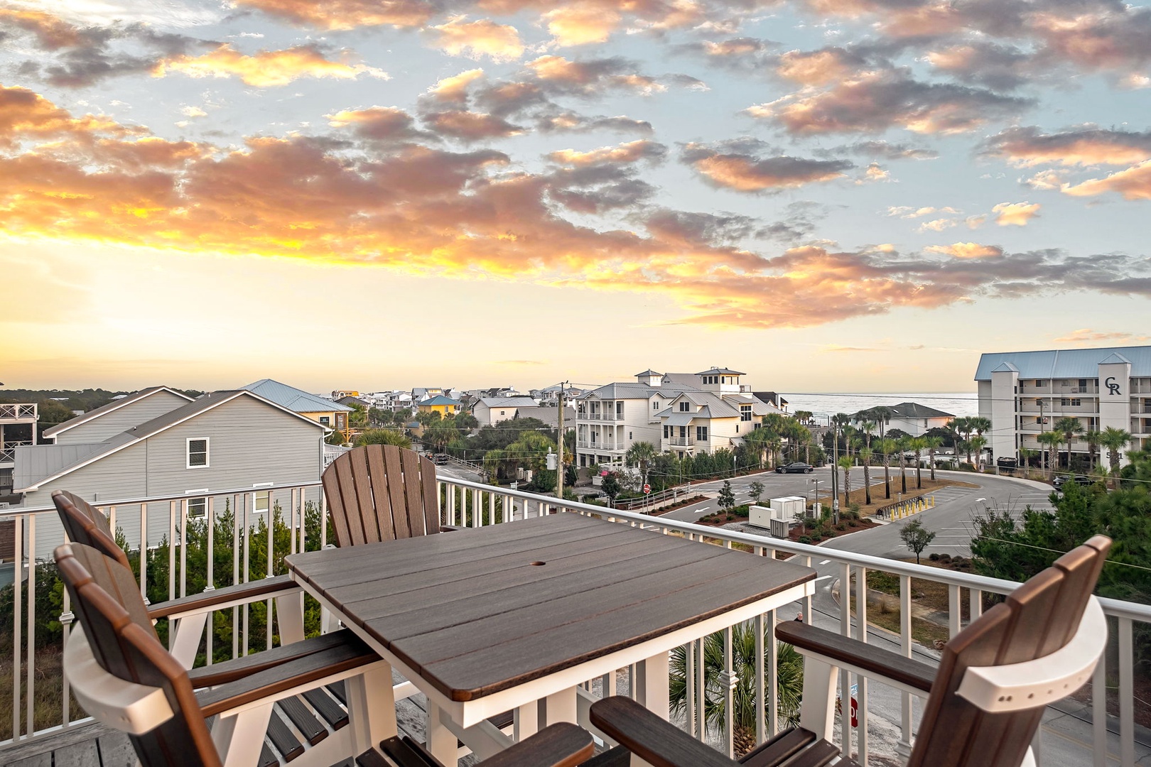 Elevated balcony with outdoor dining overlooking a coastal community during golden hour.